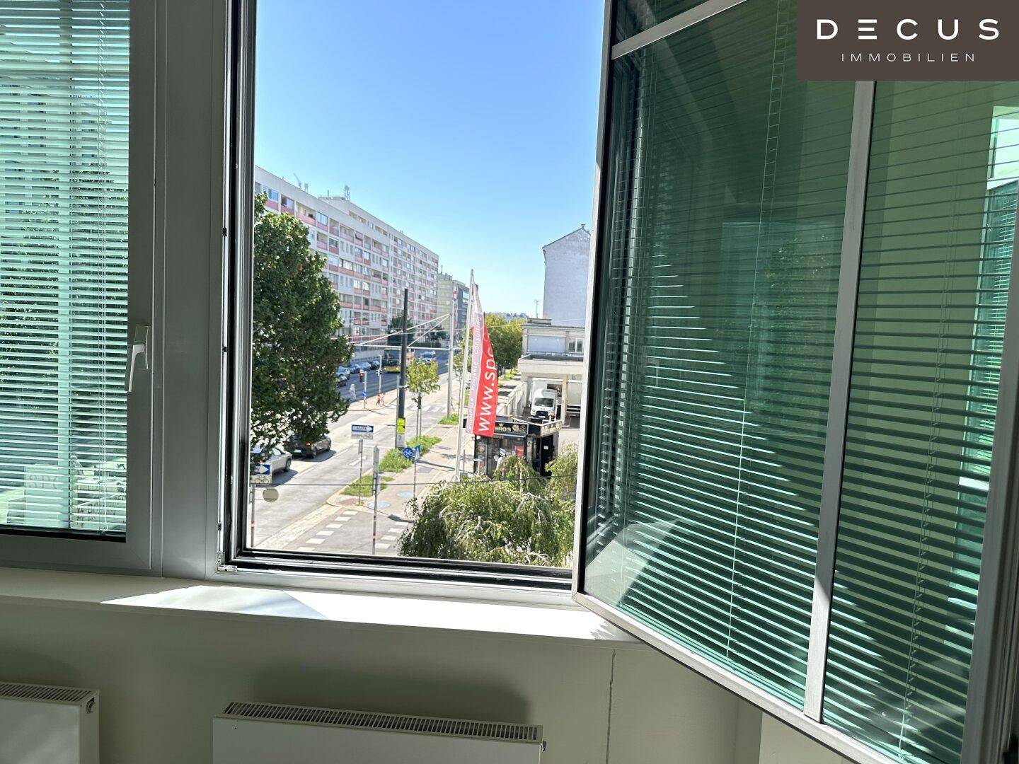 Blick aus dem Fenster eines Büros auf eine belebte Straße mit Gebäuden und Bäumen.