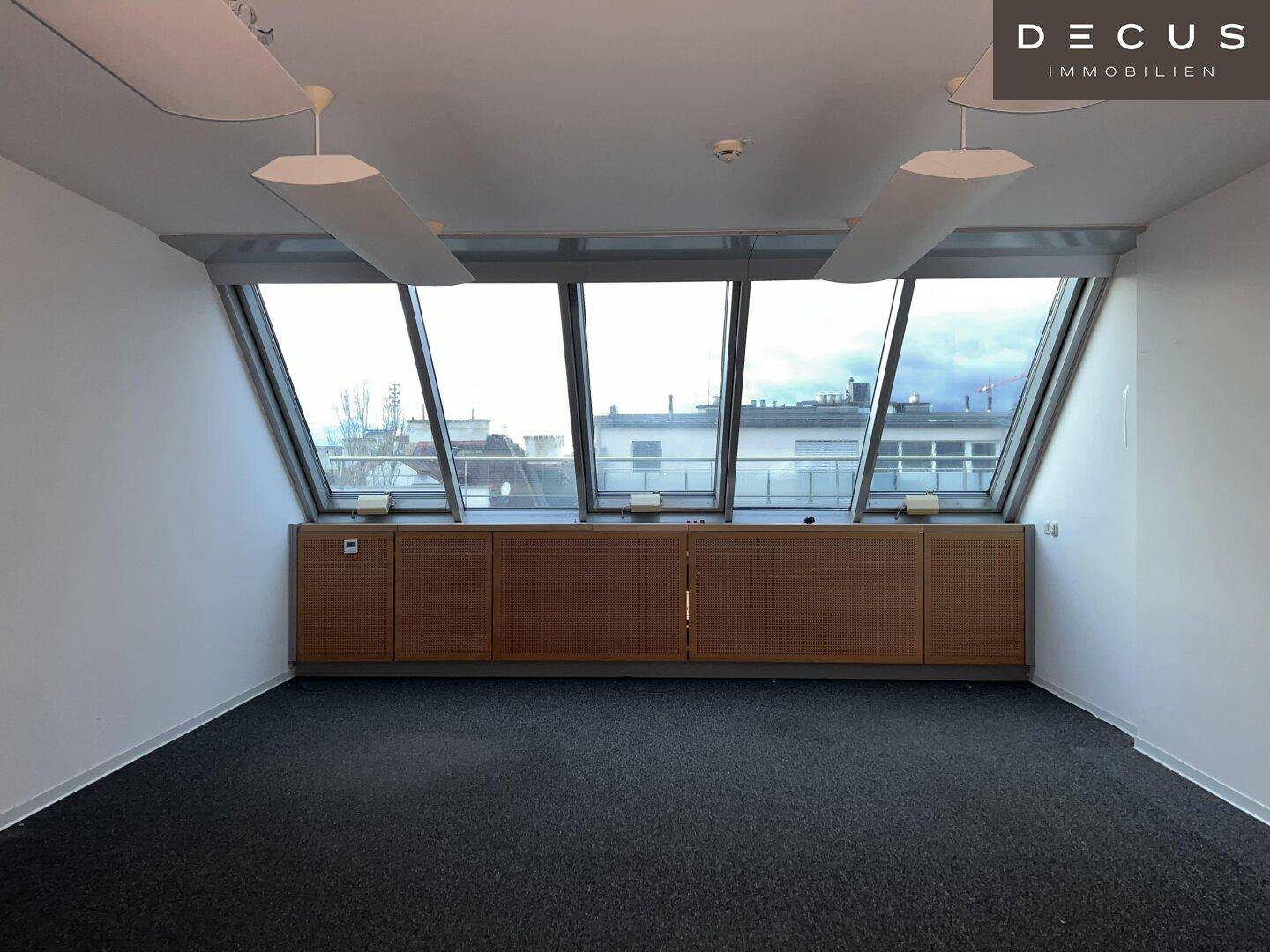 Helles Büro mit schrägen Fenstern, Einbauschränken und dunklem Teppichboden, ideal für konzentriertes Arbeiten.