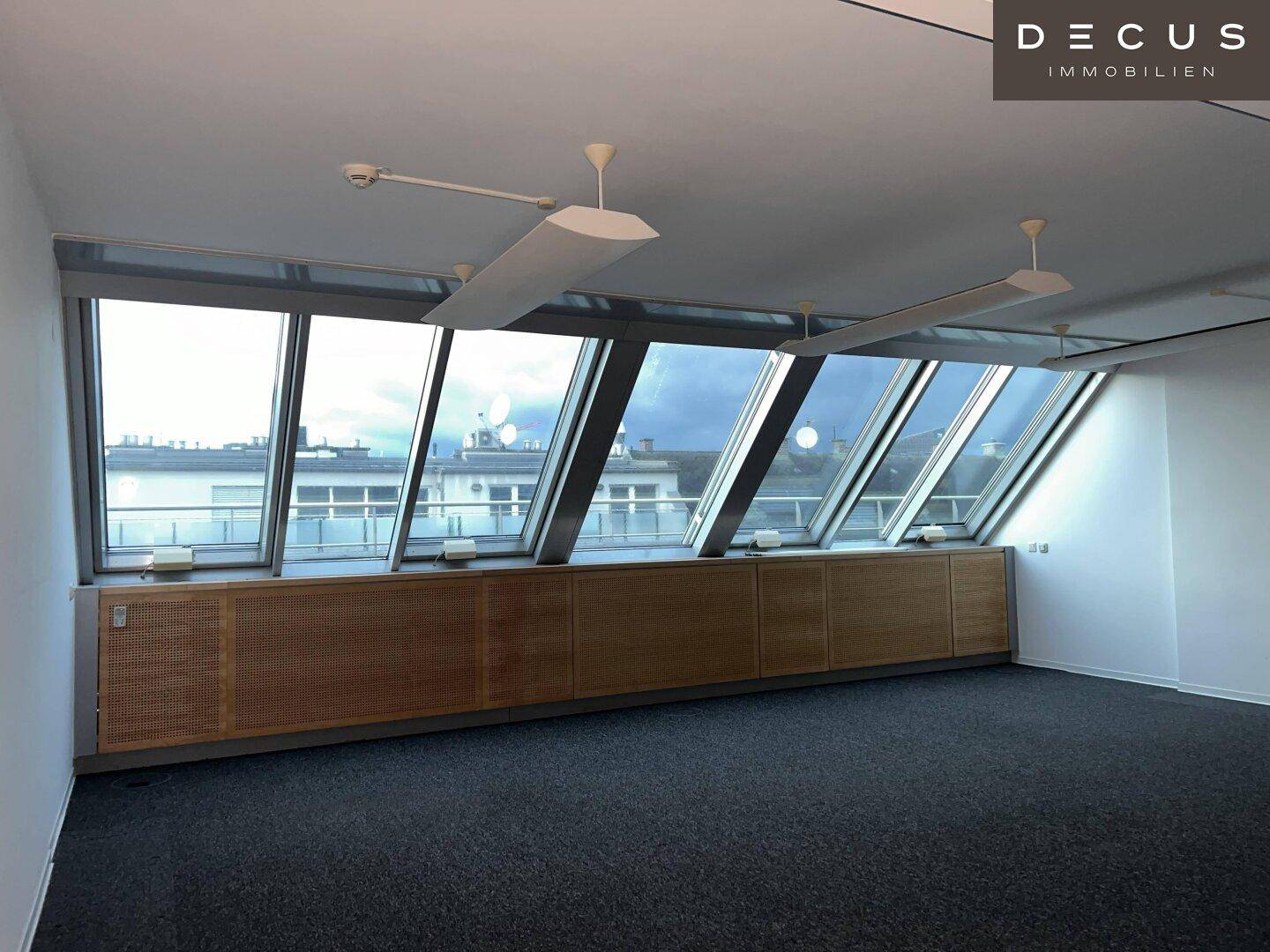 Geräumiges Büro mit schrägen Dachfenstern, integrierten Holzschränken und Teppichboden, bietet viel Tageslicht.