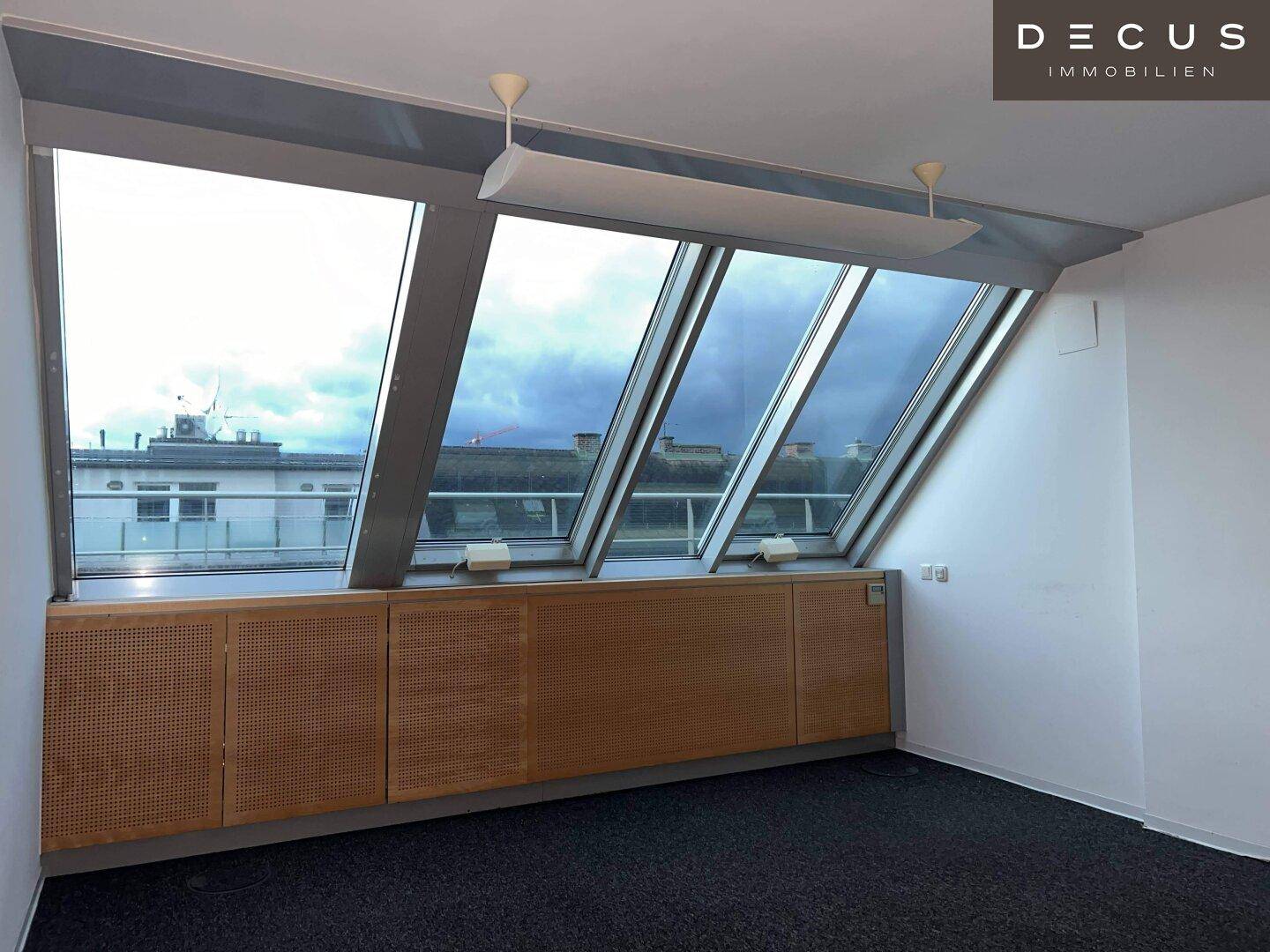 Geräumiges Büro mit schrägen Fenstern und integrierten Holzschränken, bietet eine helle Arbeitsumgebung.