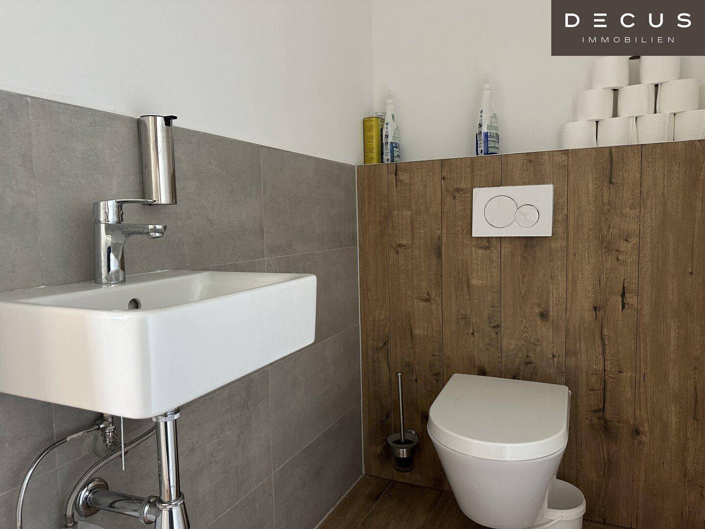 Modernes Gäste-WC mit Wand-WC, kleinem Waschbecken und einer Kombination aus Fliesen und Holzverkleidung.