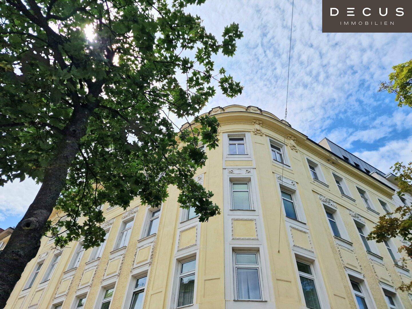 Historische Fassade eines Wohngebäudes mit vielen Fenstern und Bäumen im Vordergrund, strahlt klassischen Charme aus.