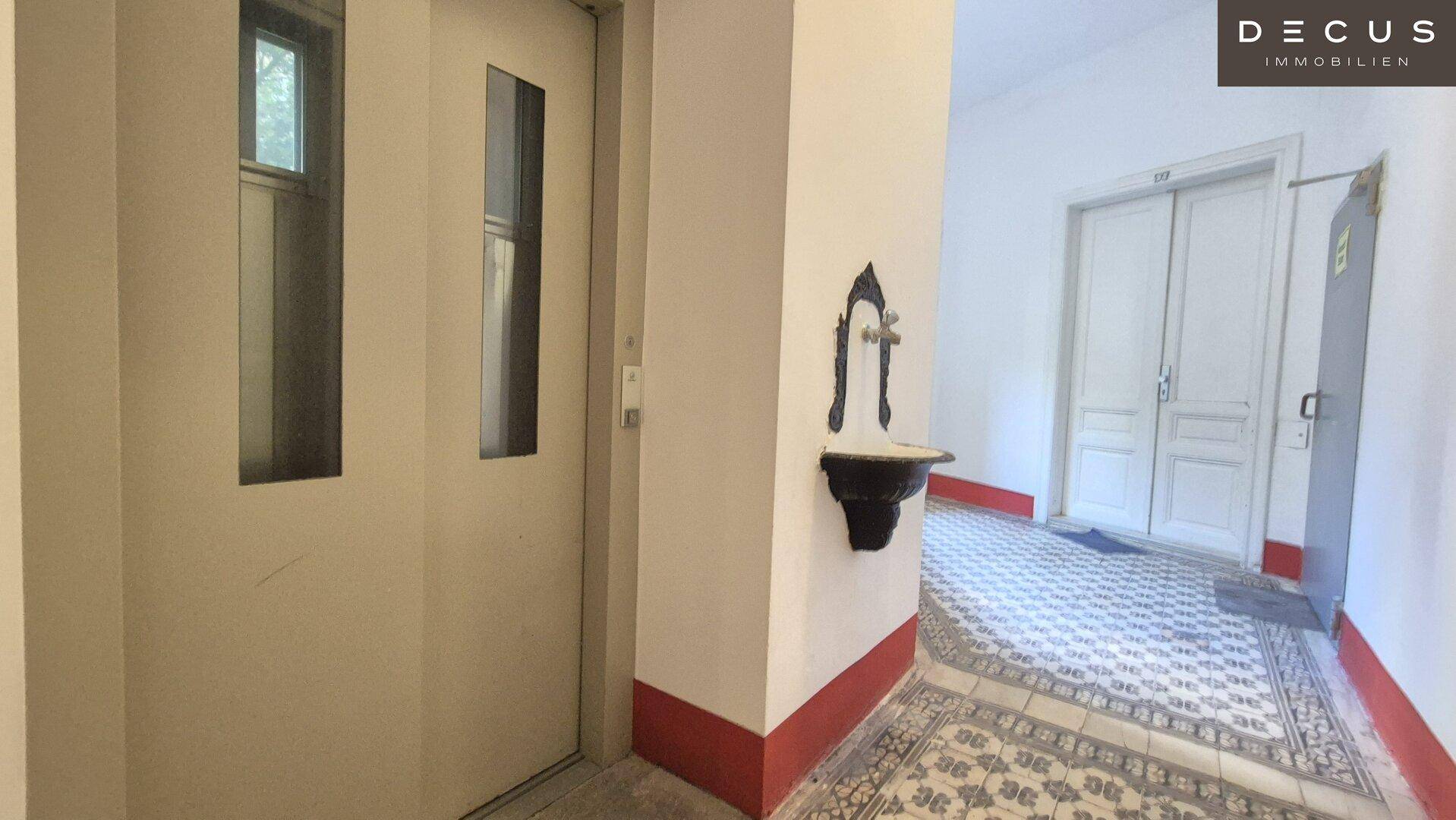 Eingangsbereich mit Aufzug, historischem Fliesenboden und dekorativem Wandbrunnen, zeugt von Altbau-Charme.