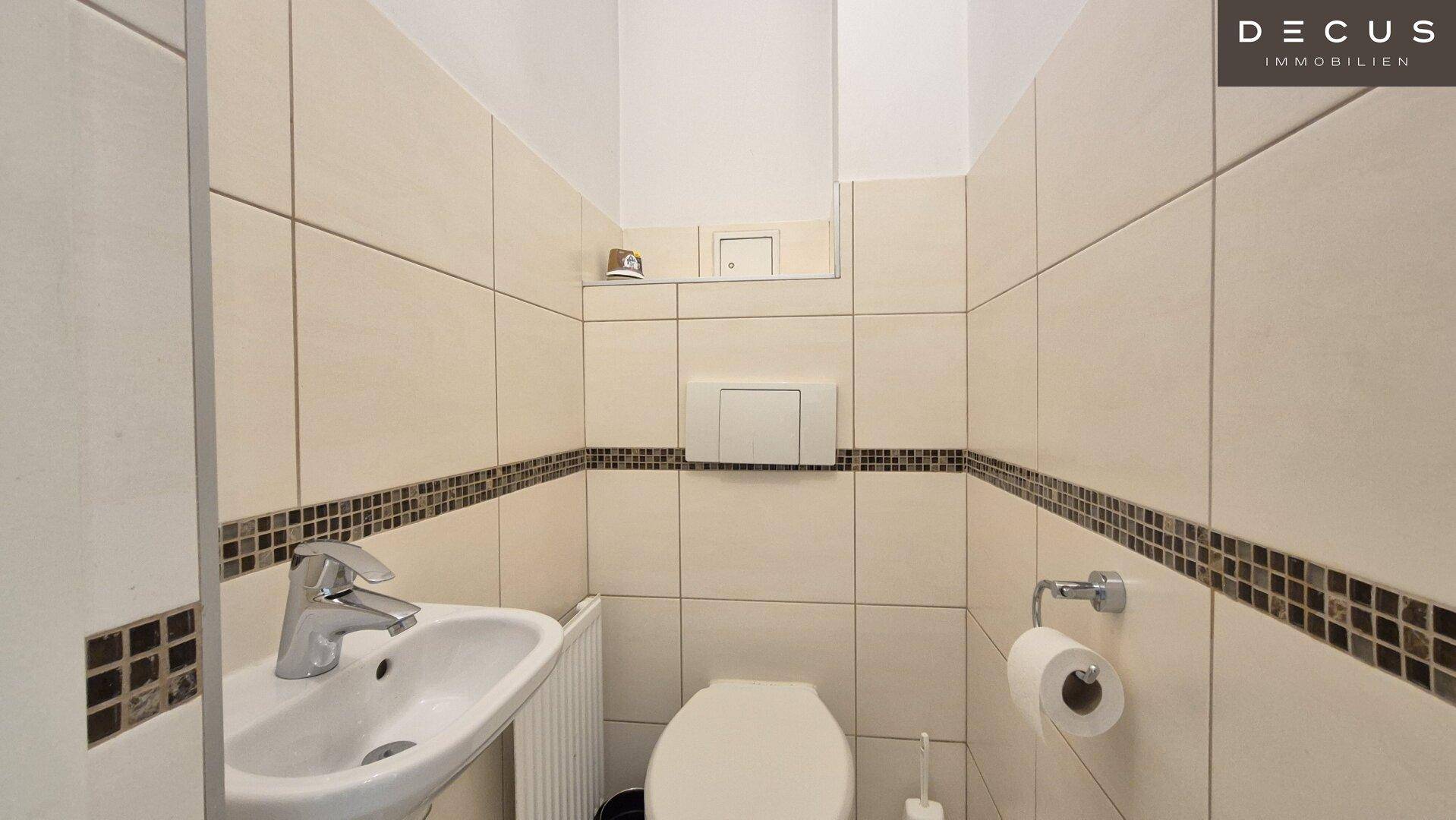Separates Gäste-WC mit Wand-WC und kleinem Waschbecken in hellen Fliesen.