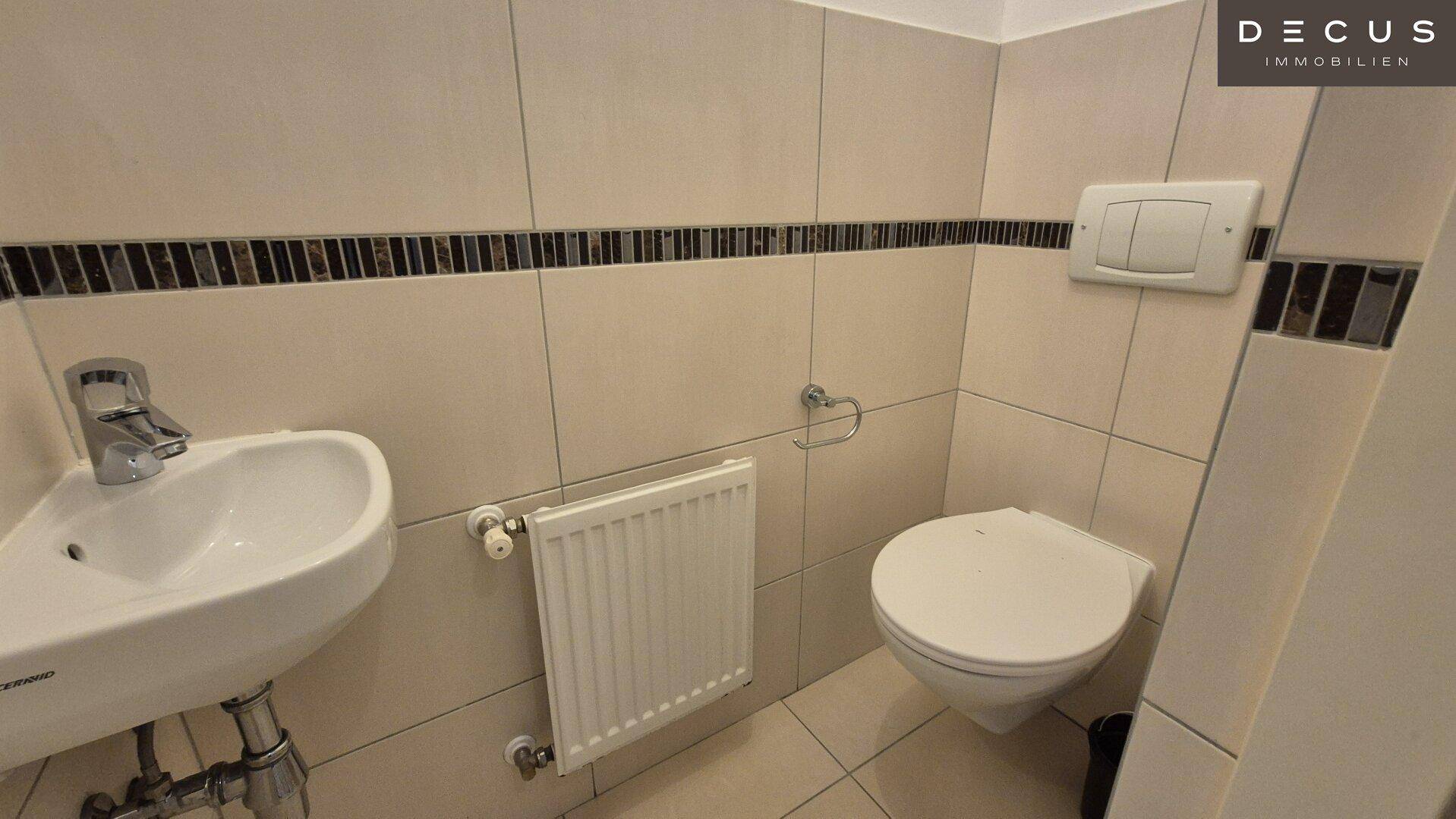 Separates WC mit wandhängender Toilette, kleinem Waschbecken und Fliesen, praktisch für Gäste.