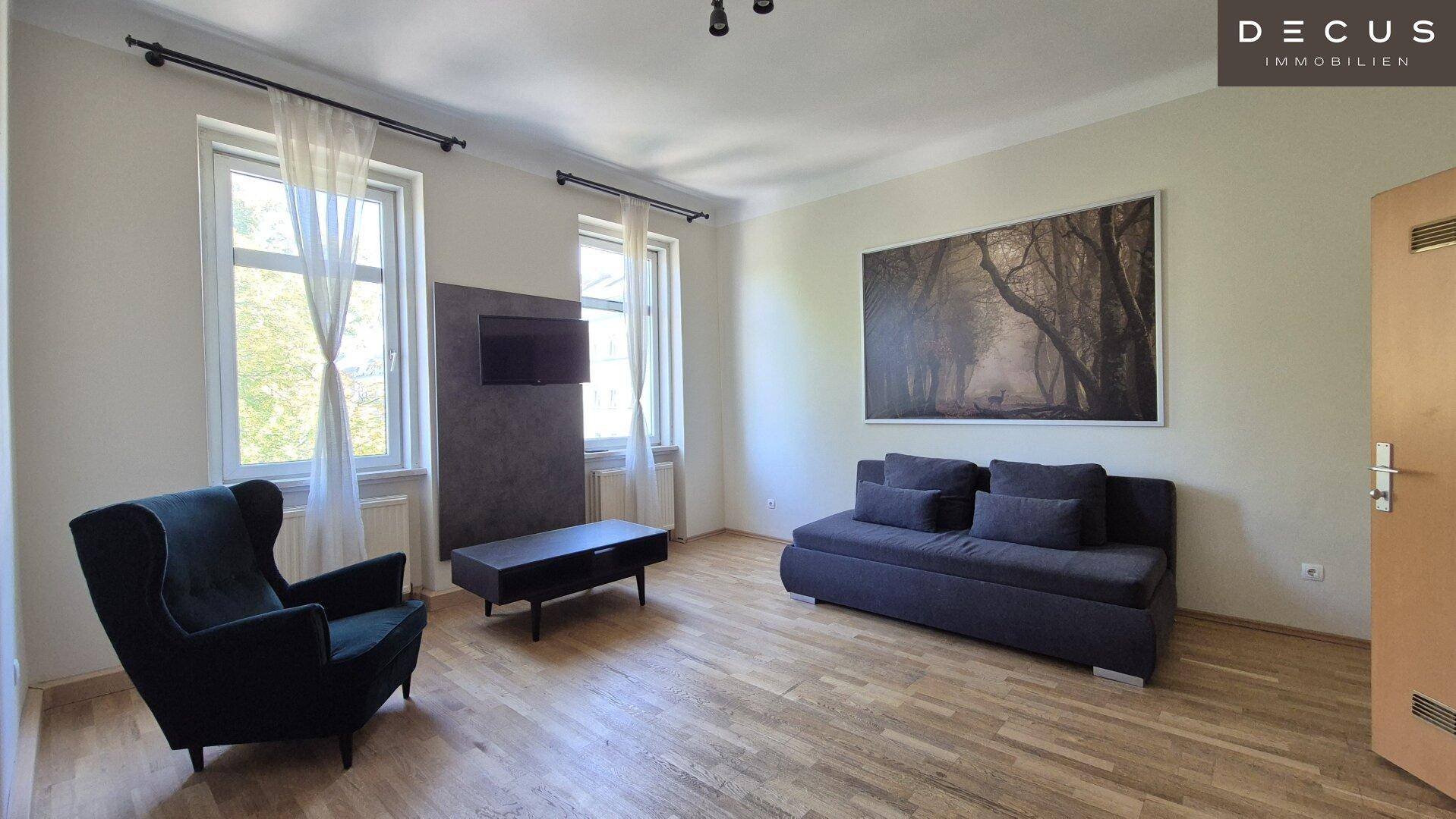 Gemütliches Wohnzimmer mit Sofa, Sessel und Fernseher, ausgestattet mit hellem Holzfußboden.