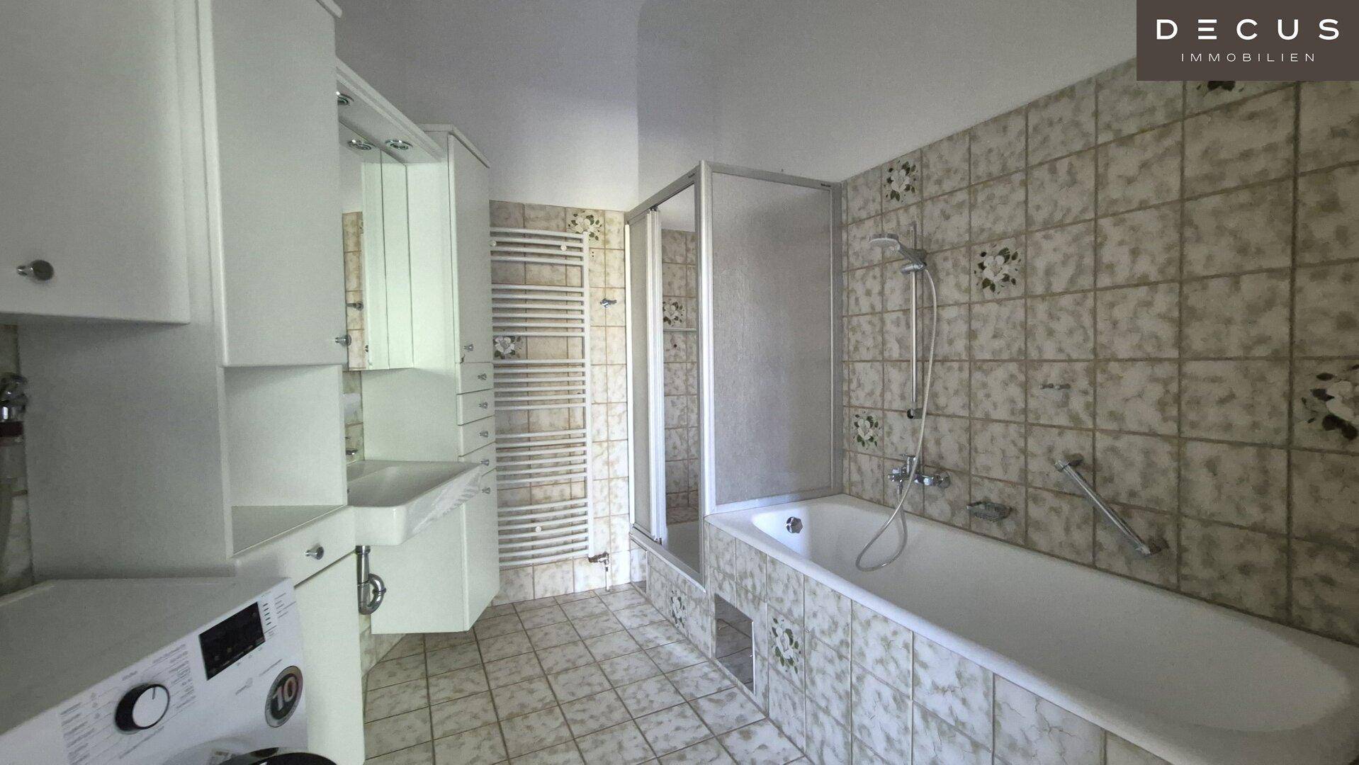 Badezimmer mit Badewanne, Duschkabine und Waschmaschine, gefliest in hellem Muster.