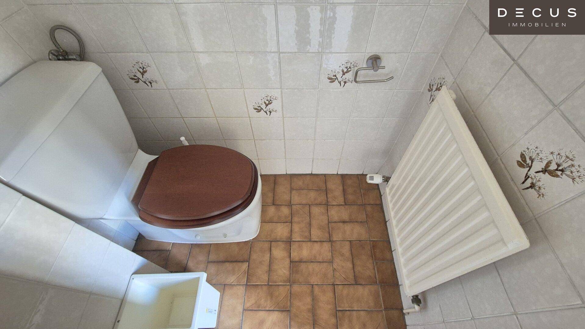 Separate Toilette mit braunem Fliesenboden und Heizkörper, einfach und funktional gestaltet.