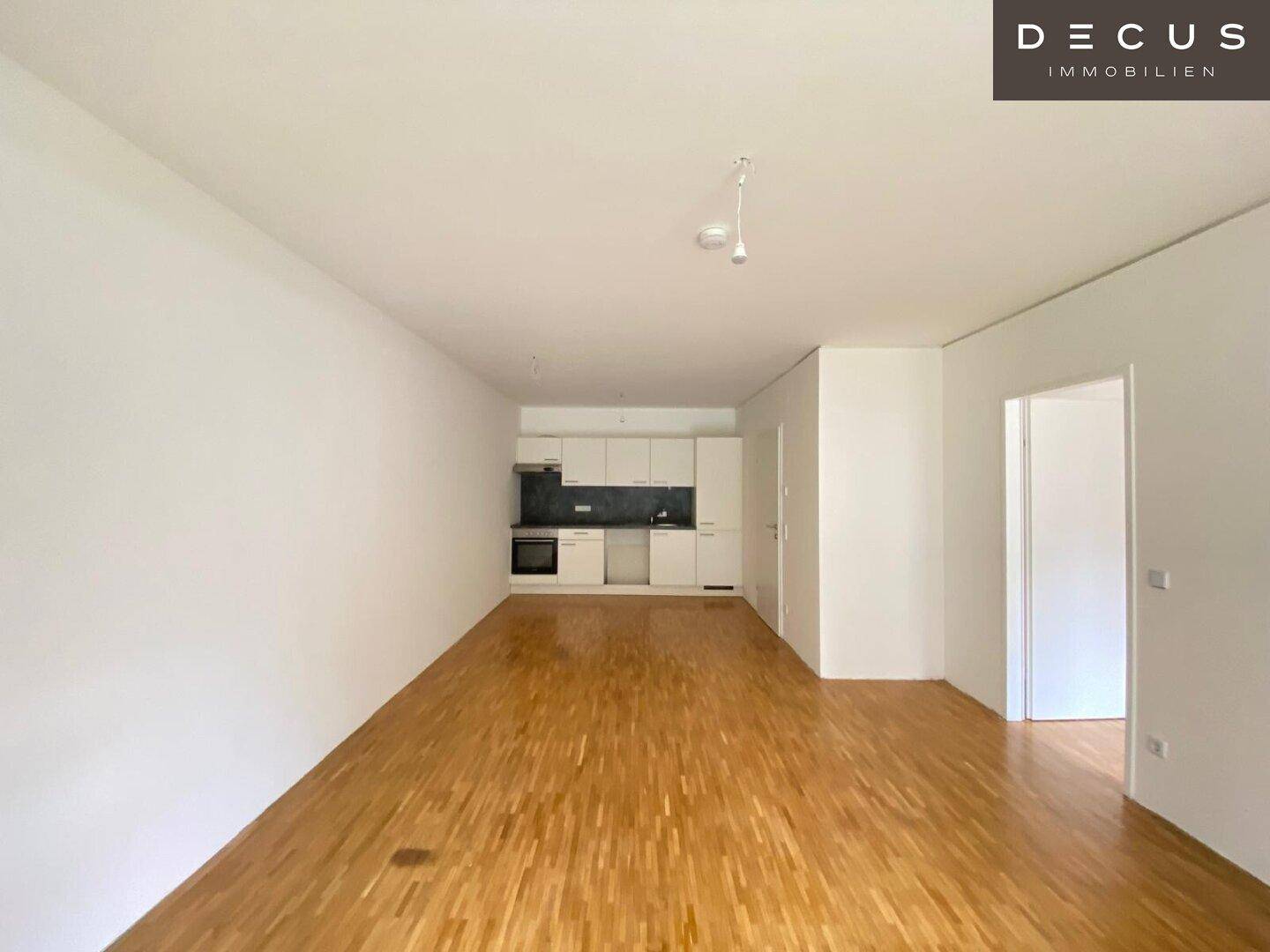 Offener Wohnbereich mit integrierter weißer Küchenzeile und Parkettboden, ideal für modernes Wohnen.
