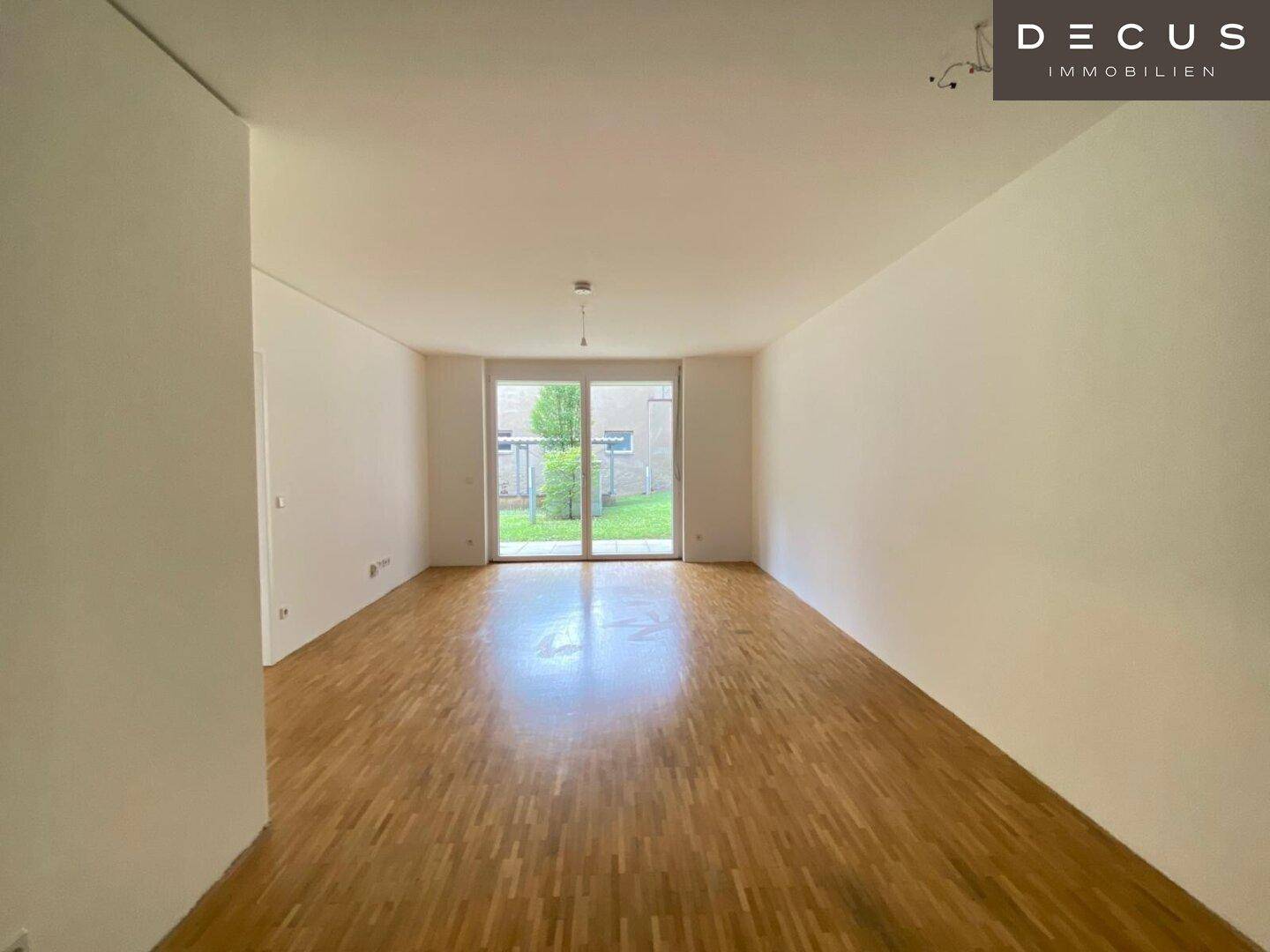 Heller Wohnraum mit Holzboden und großem Fenster, das den Blick in den Garten freigibt.
