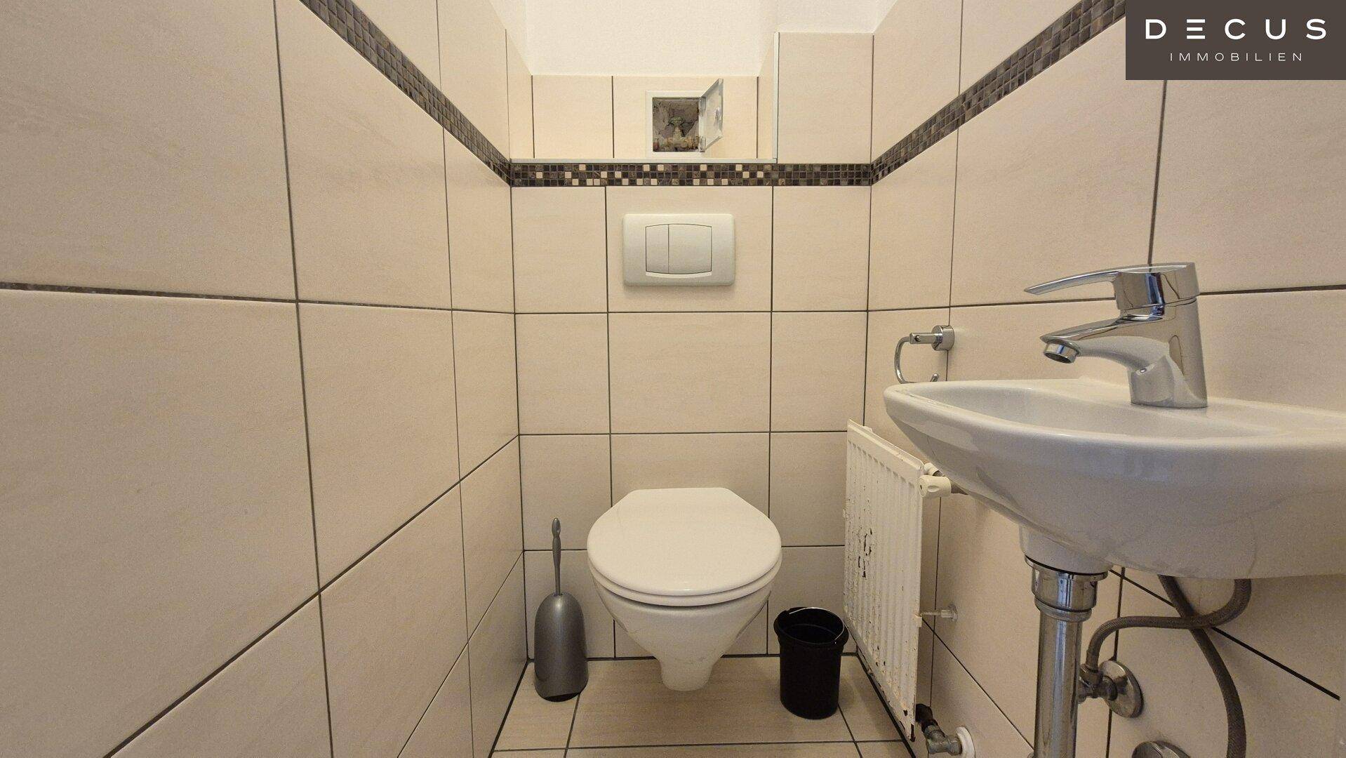 Kleines Gäste-WC mit Wand-WC, Waschbecken und hellen Fliesen an den Wänden.