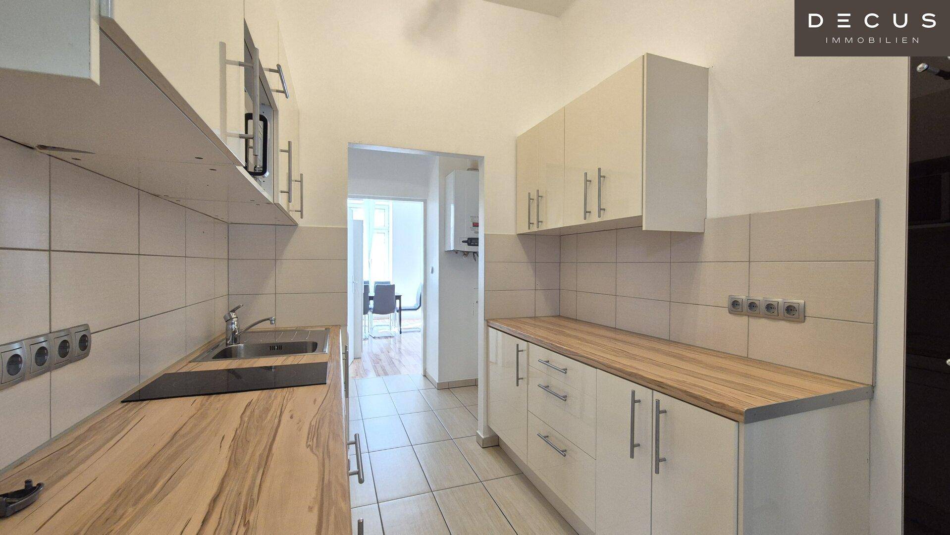 Funktionale Küche mit hellen Schränken, Holz-Arbeitsplatten und gefliestem Spritzschutz.