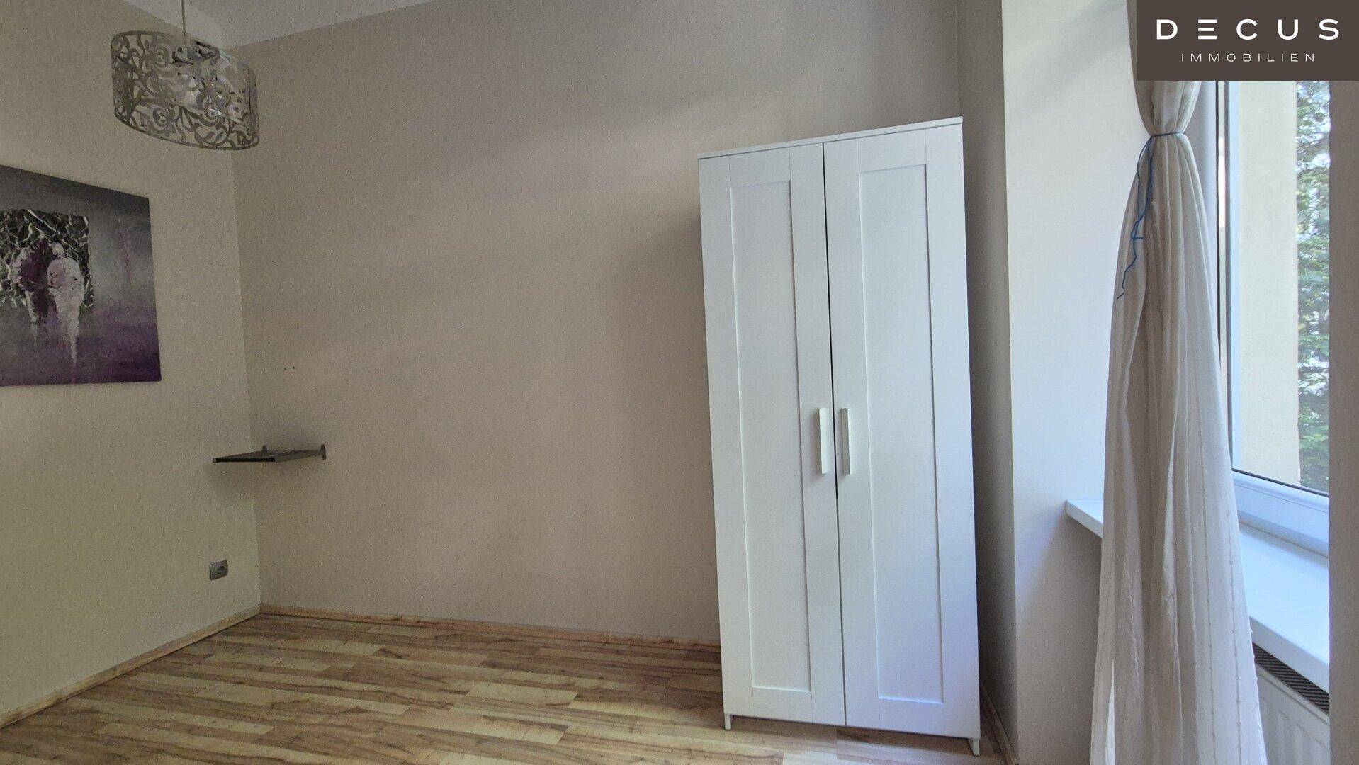 Schlafzimmer mit Parkettboden, weißem Kleiderschrank und großem Fenster für viel Tageslicht.