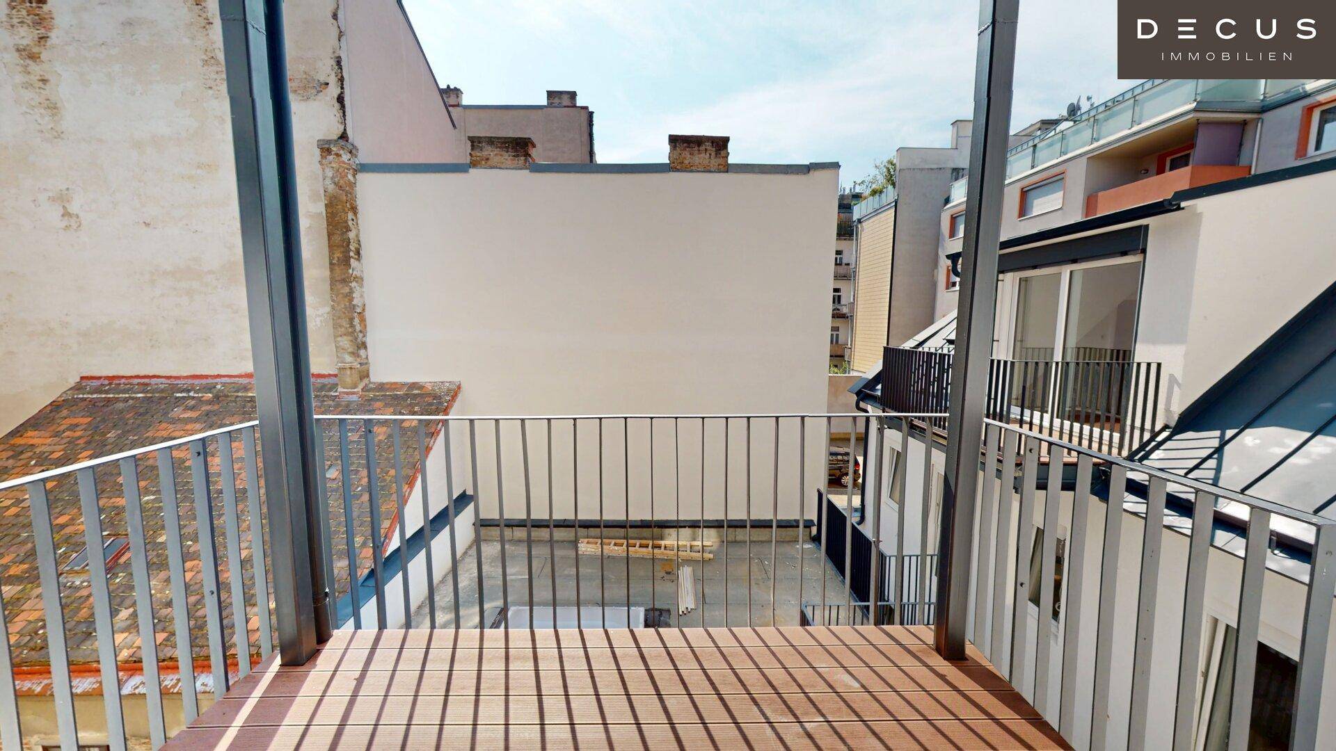 Geräumige Terrasse mit Holzboden und Metallgeländer, bietet einen Blick auf den Innenhof.