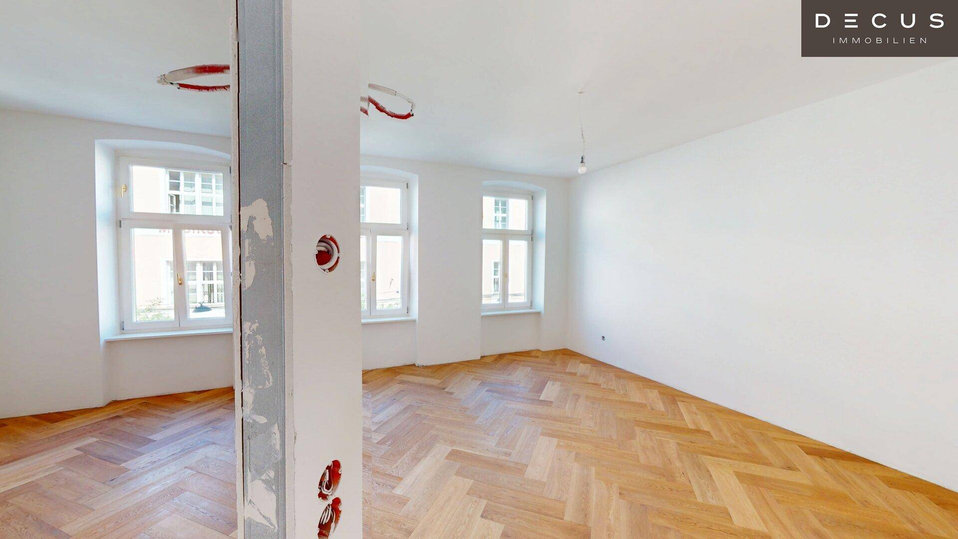 Heller Raum mit Fischgrätparkett und mehreren Fenstern, bereit für den Innenausbau.