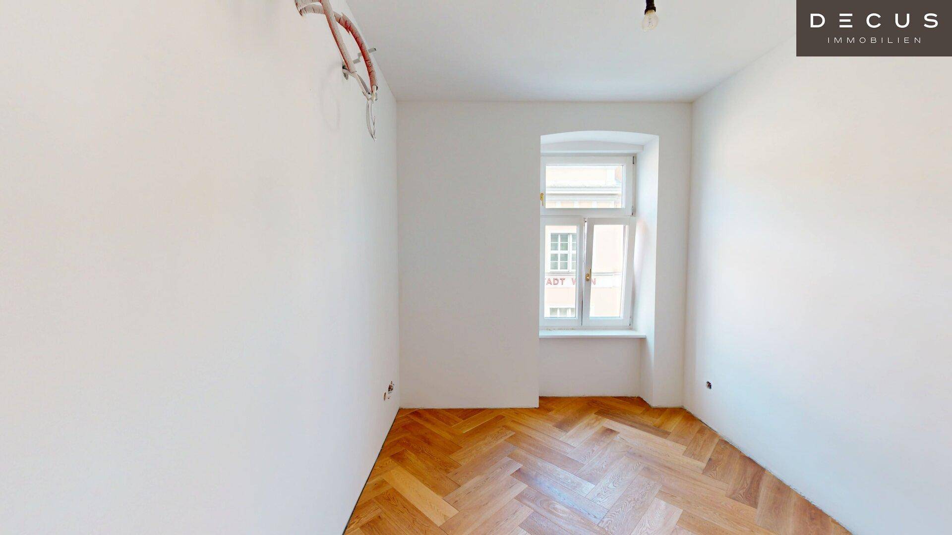 Heller Raum mit Fischgrätparkett und einem Fenster, mit sichtbaren Installationsvorbereitungen.