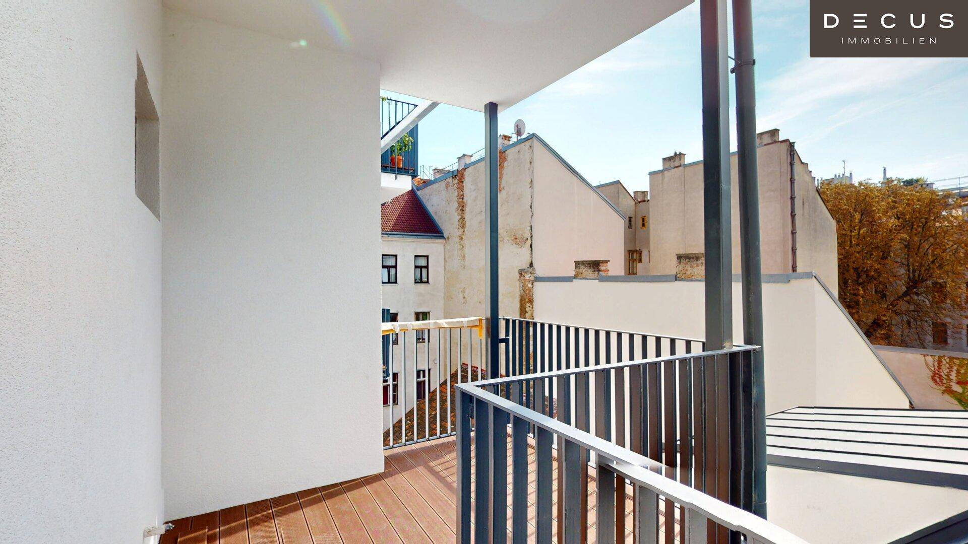 Moderner Balkon mit Holzbelag und Metallgeländer, bietet einen Blick auf die umliegenden Gebäude.