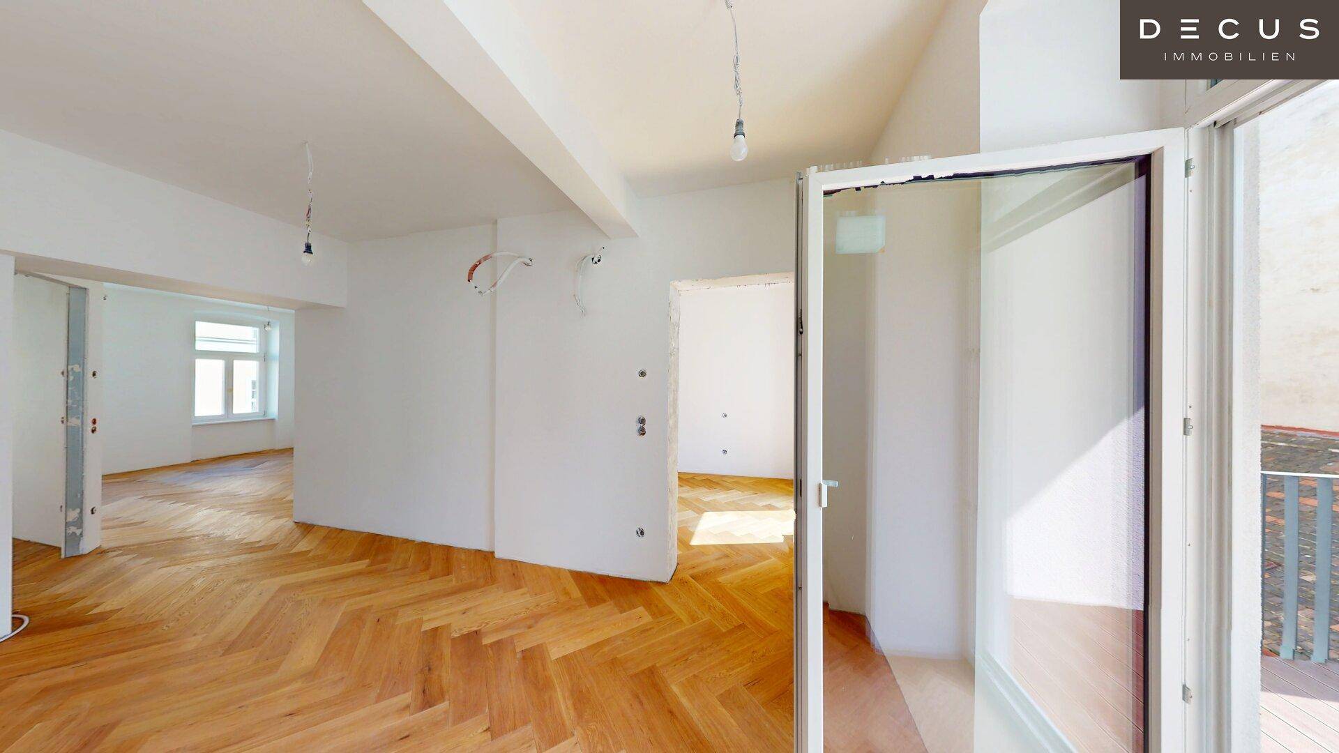 Geräumiger Raum im Rohbau mit Fischgrätparkett und Zugang zu einem Balkon mit Innenhofblick.