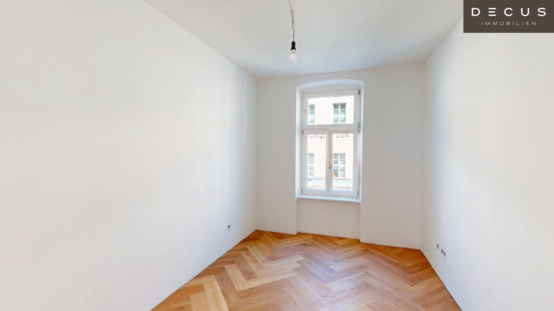 Helles Schlafzimmer im Rohbau mit Fischgrätparkett und einem Fenster, bereit für die individuelle Gestaltung.