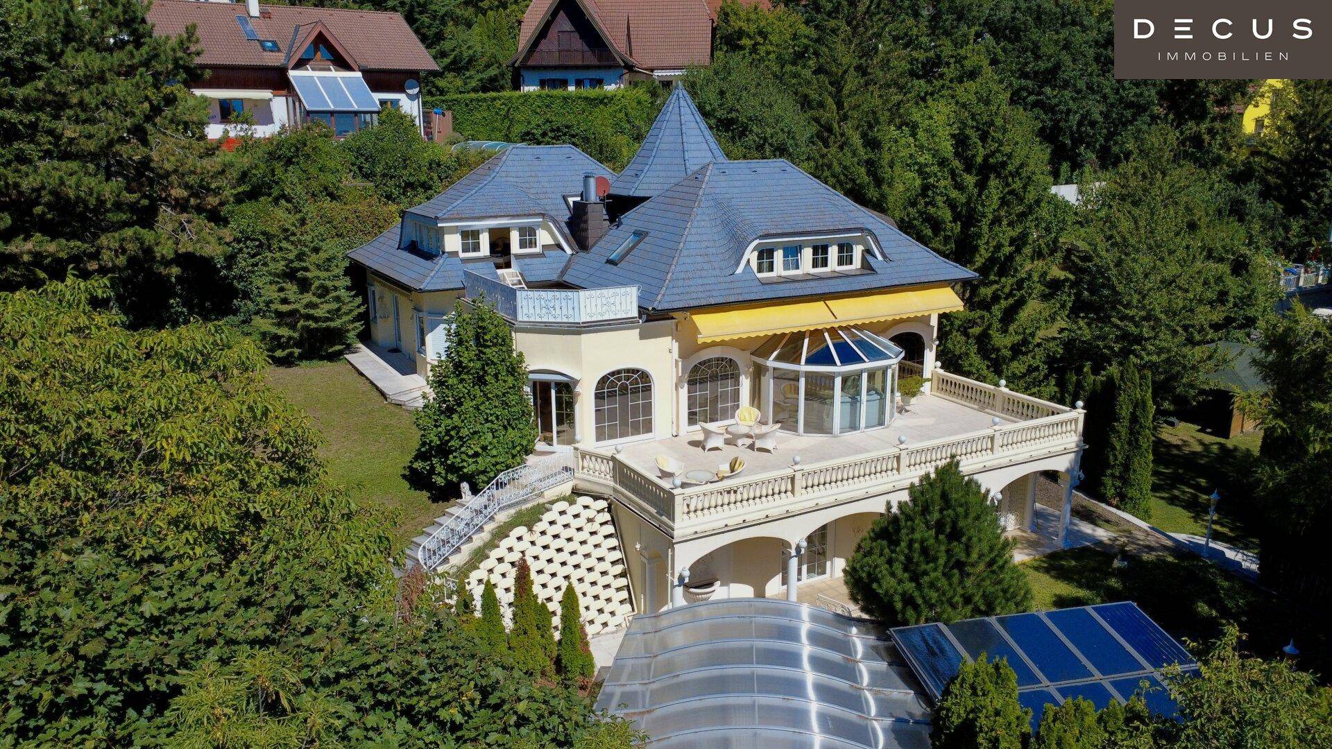 Historische Villa mit Mansarddach und großzügiger Terrasse, umgeben von üppigem Grün.