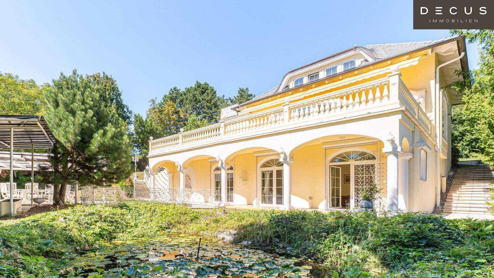 Elegante Fassade der Villa mit Arkaden und einem idyllischen Teich im Vordergrund.