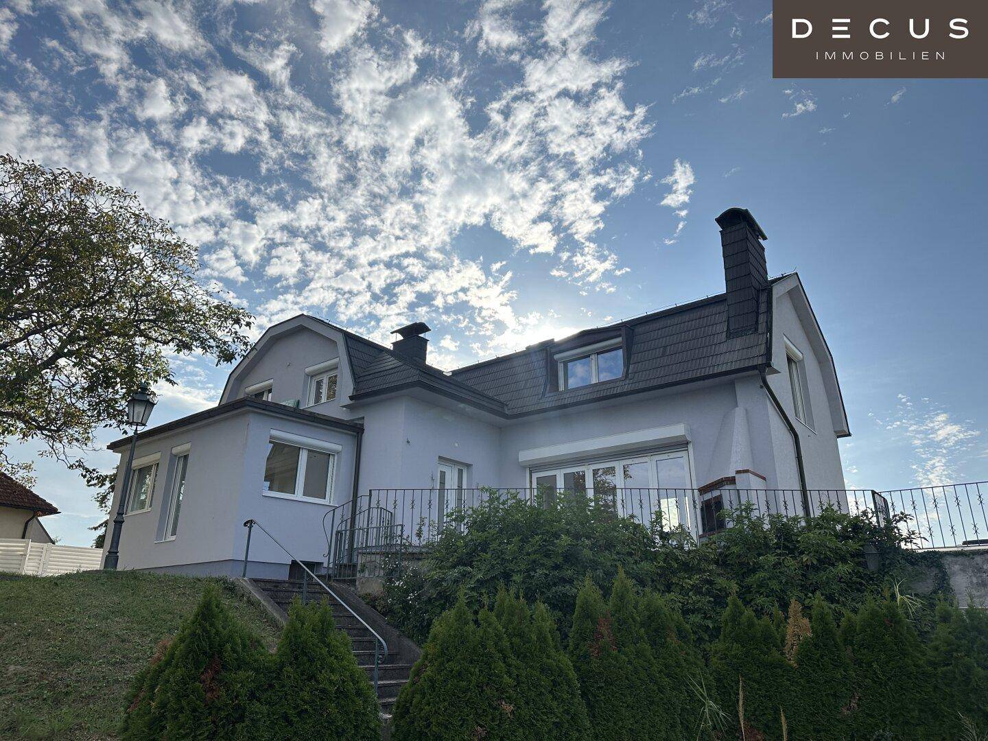 Ansicht des Hauses mit Mansarddach, großen Fenstern und gepflegter Außenanlage.