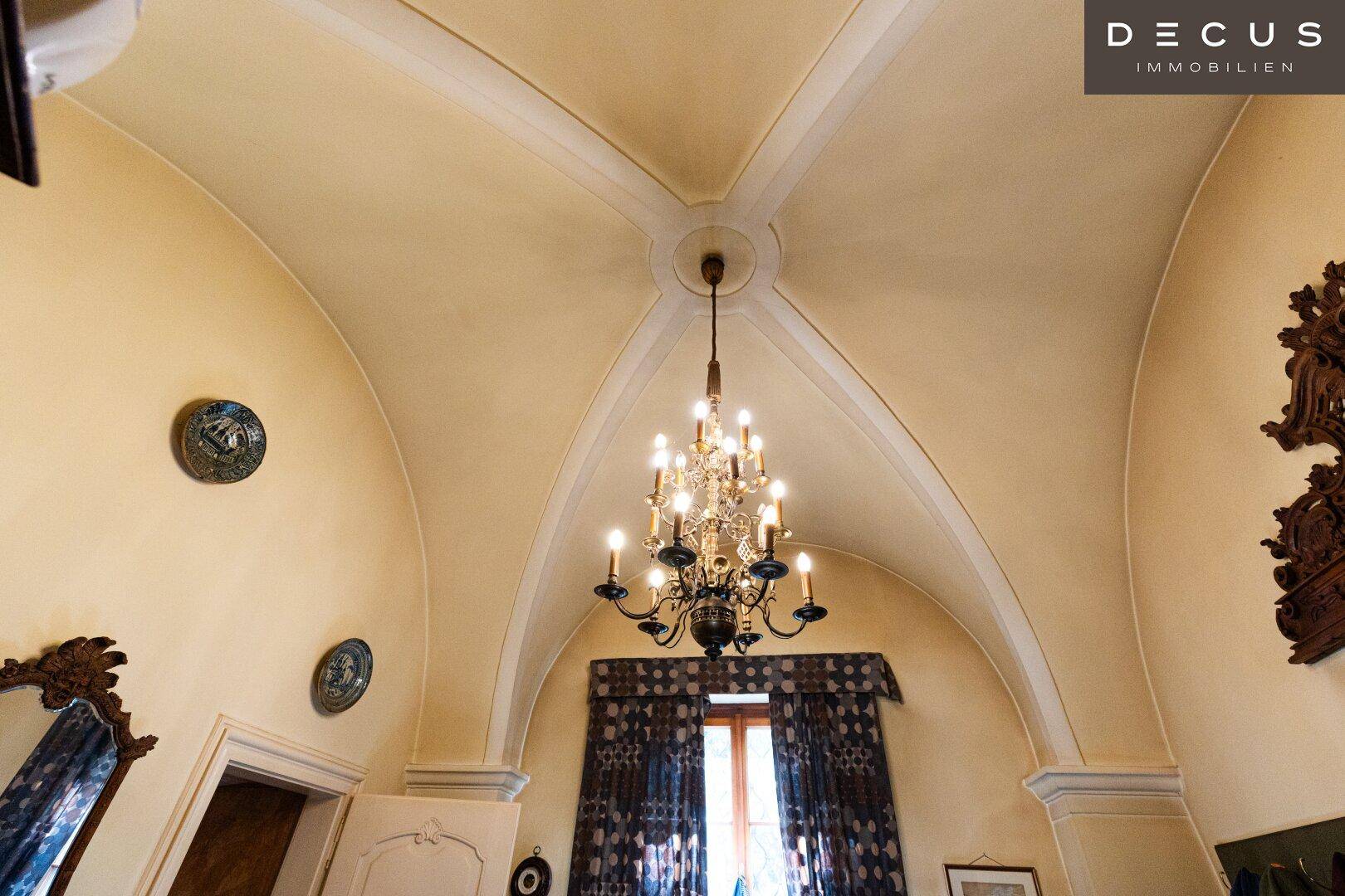 Gewölbte Decke mit elegantem Kronleuchter und traditioneller Dekoration in einem historischen Raum.