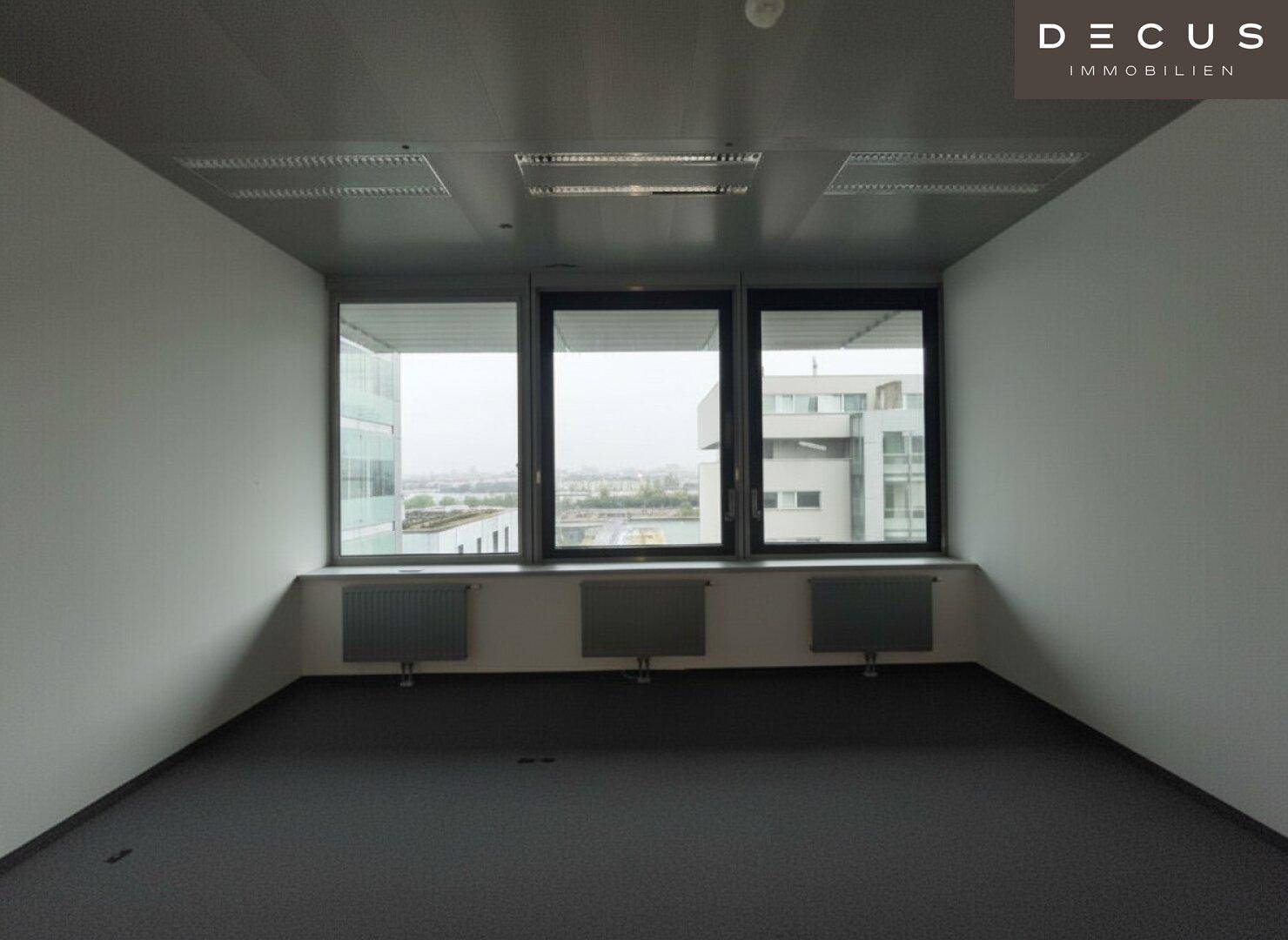 Heller Büroraum mit Teppichboden und drei großen Fenstern, die einen weiten Blick bieten.