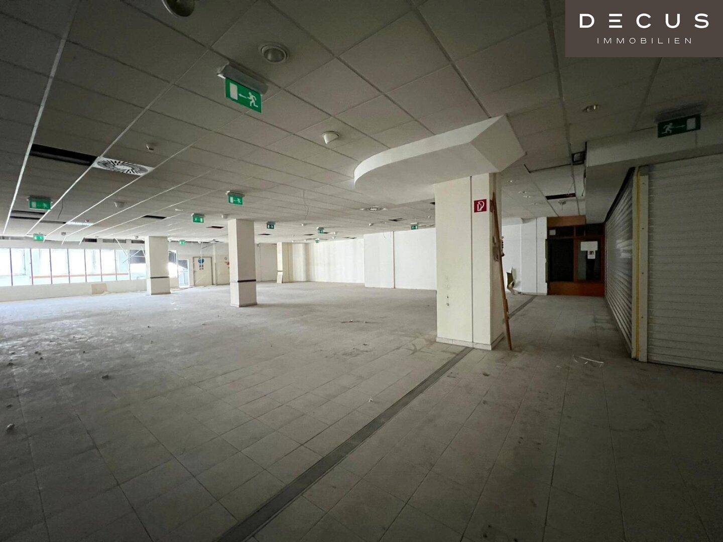 Großer, leerer Gewerberaum mit Fliesenboden, Säulen und abgehängter Decke, bereit für den Ausbau.
