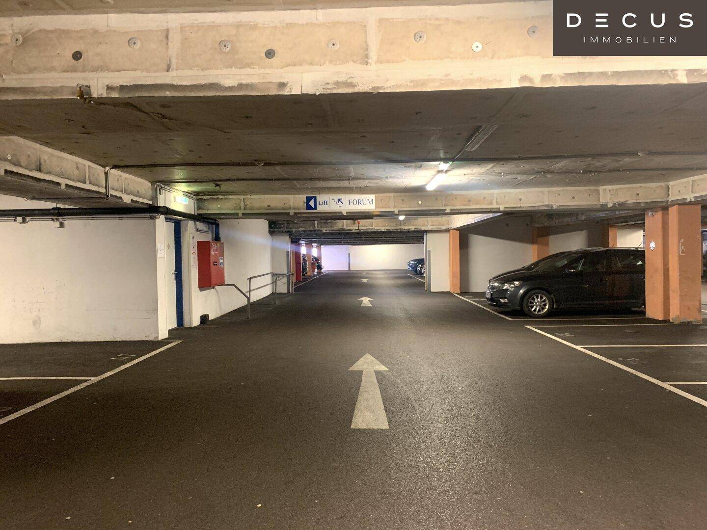 Innenansicht einer Tiefgarage mit Betonstruktur, markierten Parkplätzen und geparkten Fahrzeugen.