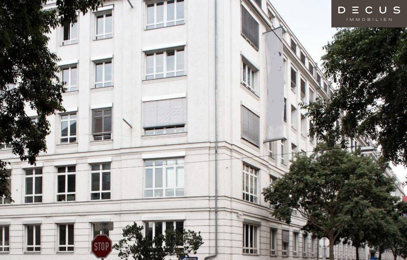 Mehrstöckiges Bürogebäude mit vielen Fenstern und Jalousien, umgeben von Bäumen an einer Straße.