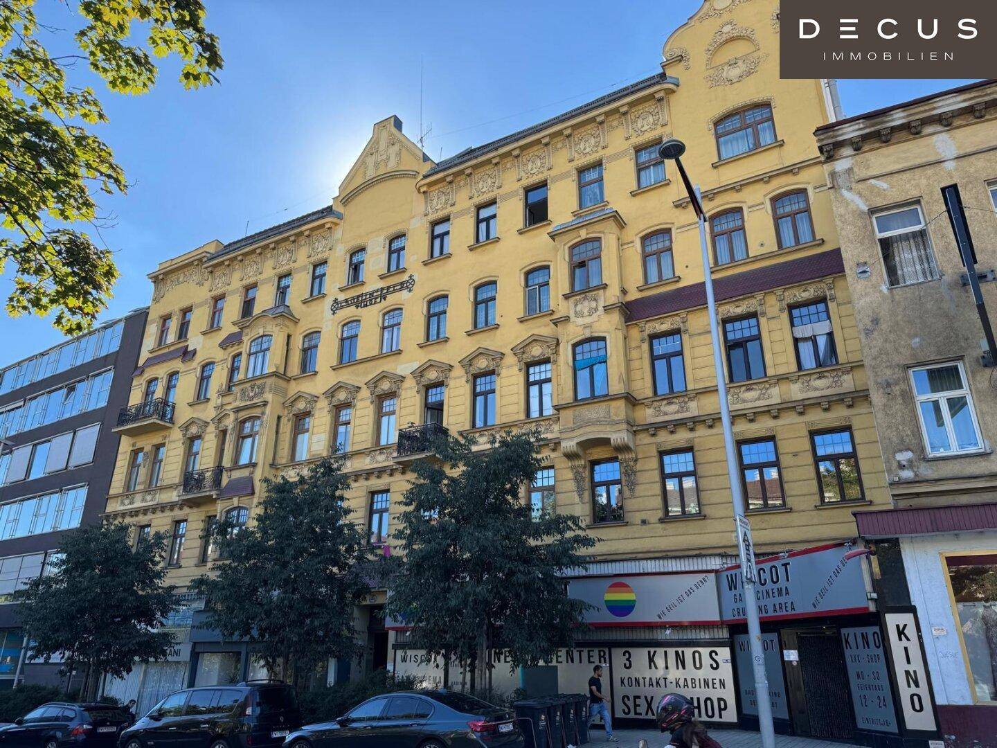 Mehrstöckiges Gebäude mit gelber Fassade, vielen Fenstern und Geschäften im Erdgeschoss an einer belebten Straße.