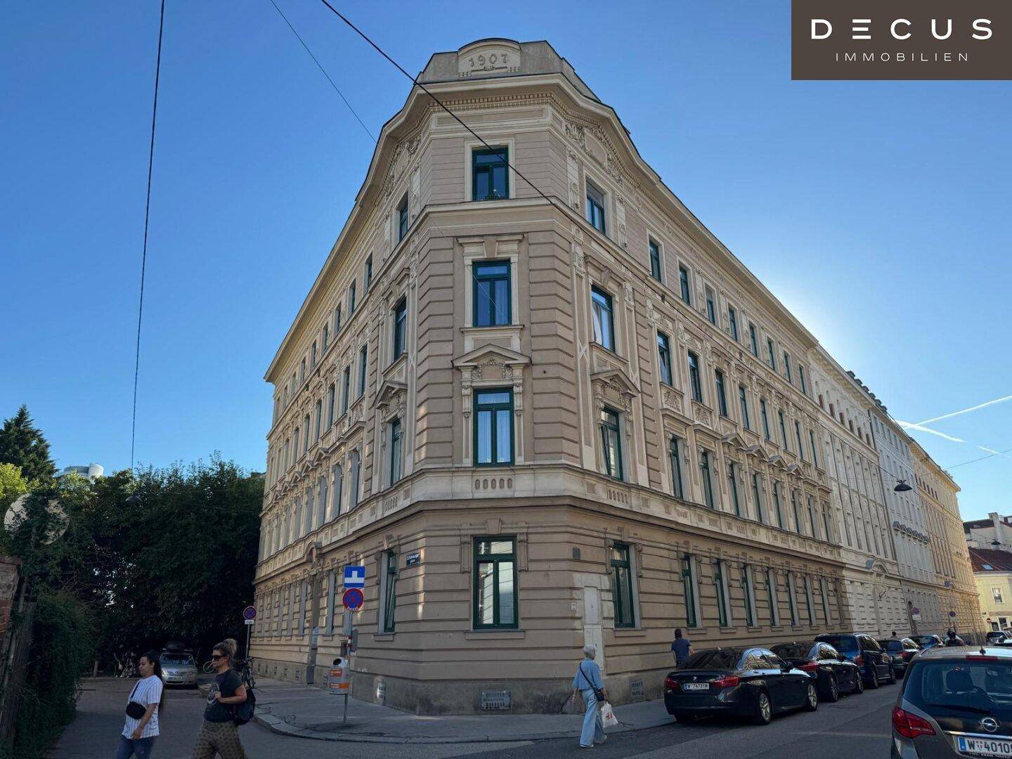 Historisches Eckgebäude mit markanter Architektur und grünen Fensterrahmen unter blauem Himmel in der Stadt.