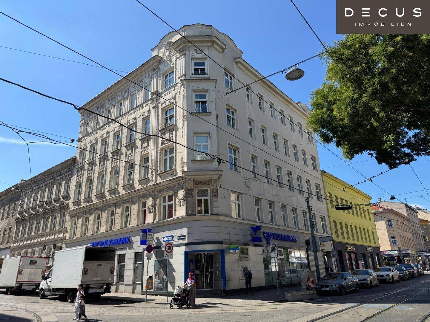 Großes Eckgebäude mit weißer Fassade und einer Bankfiliale im Erdgeschoss an einer städtischen Kreuzung.