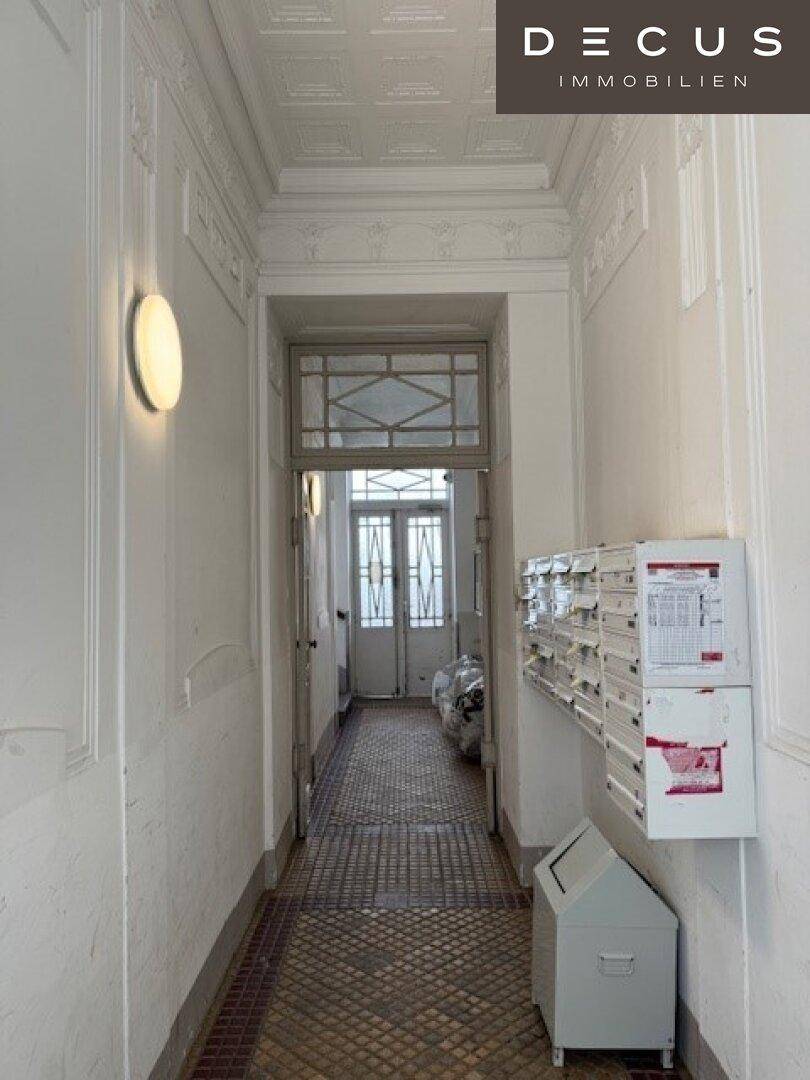 Heller Hausflur mit dekorierter Stuckdecke, gemustertem Fliesenboden und Briefkästen.