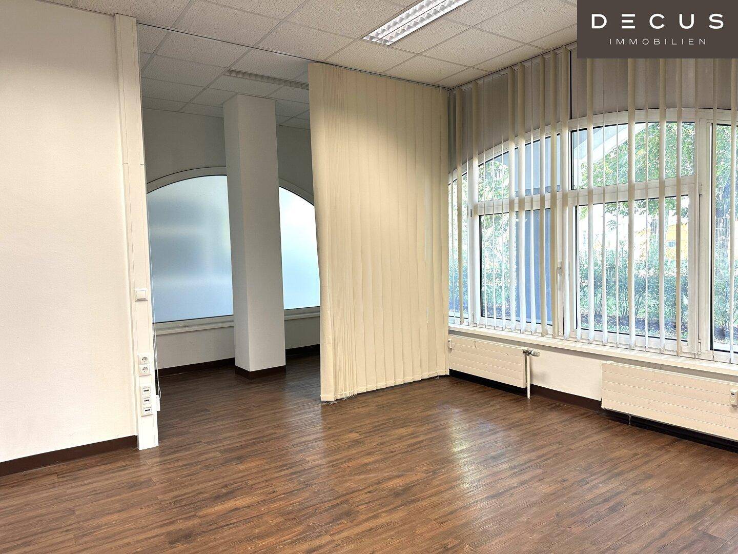 Geräumiger, heller Büroraum mit Holzboden und großen Fenstern, die viel Tageslicht hereinlassen.