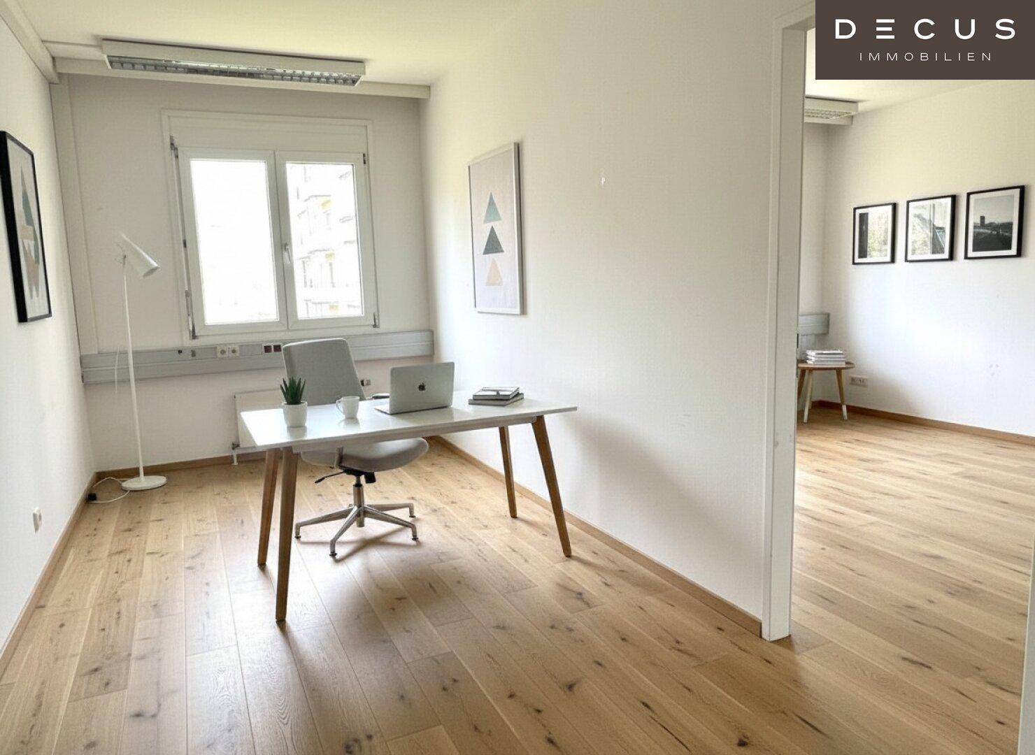Einzelbüro mit einem Arbeitsplatz, Holzboden und einer Trennwand zu einem angrenzenden Raum.
