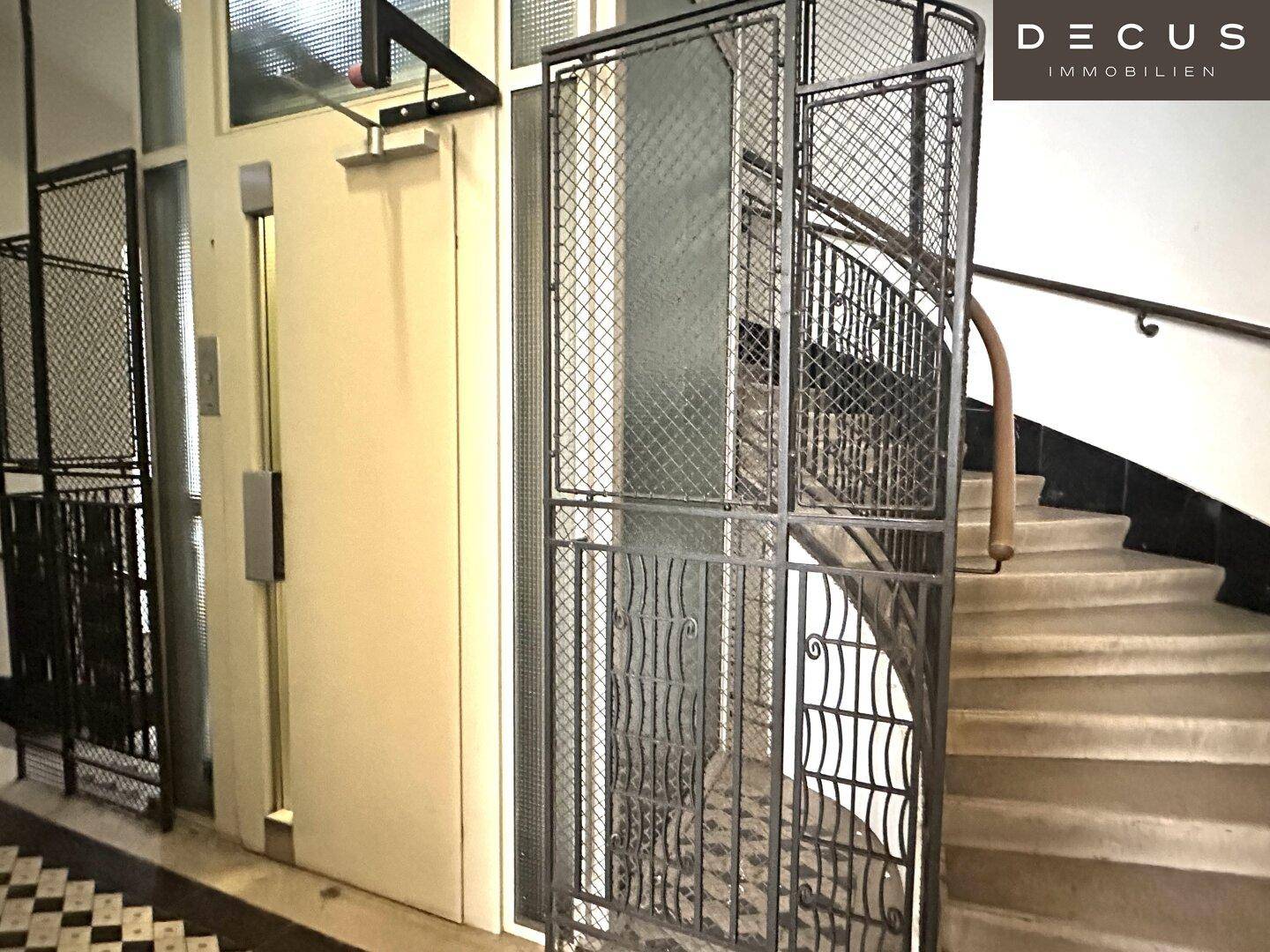 Detailansicht des historischen Gitteraufzugs neben der Treppe im Eingangsbereich des Gebäudes.
