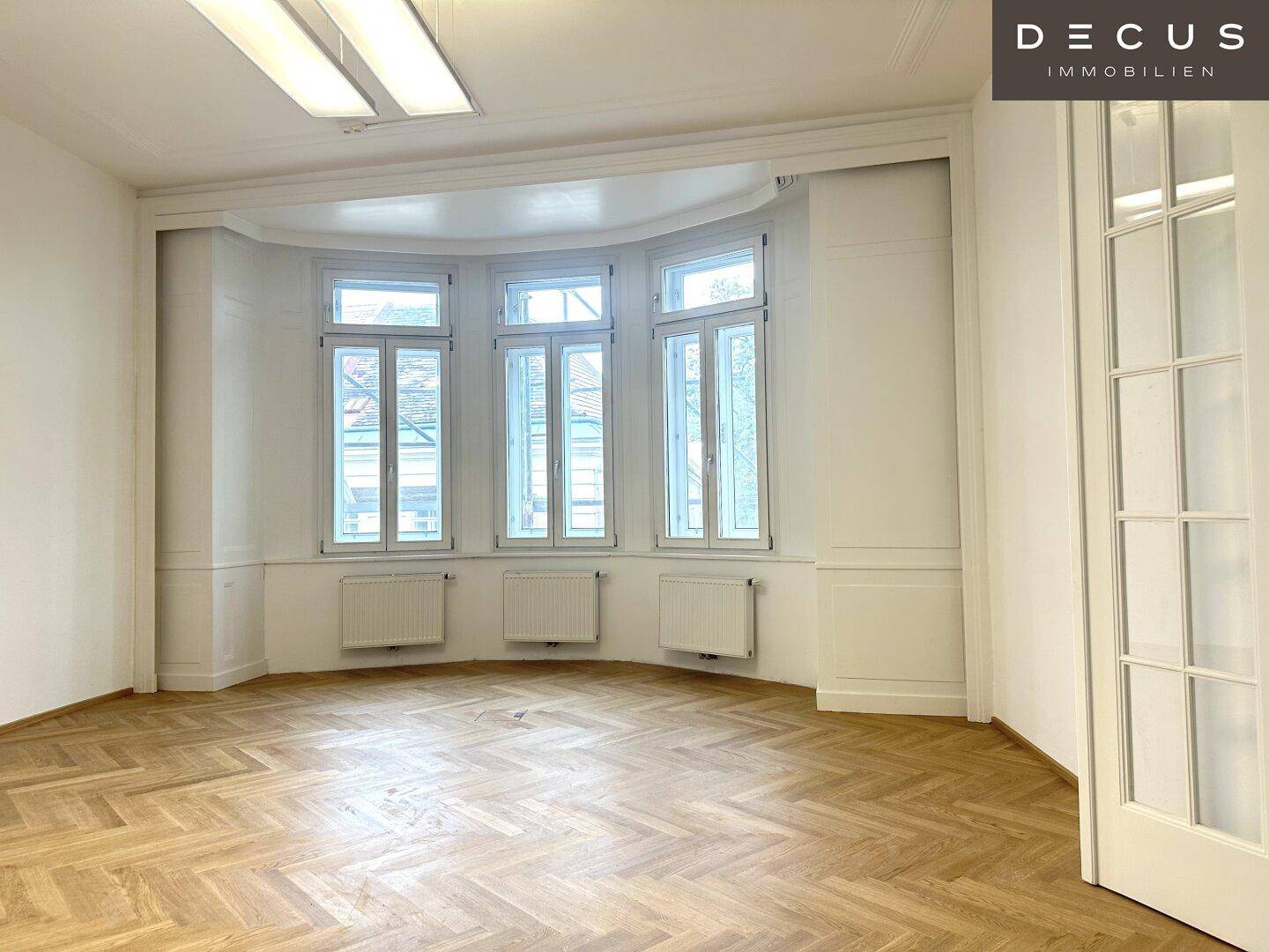 Eleganter Raum mit Fischgrätparkett und einem markanten Erkerfenster, das viel Licht spendet.