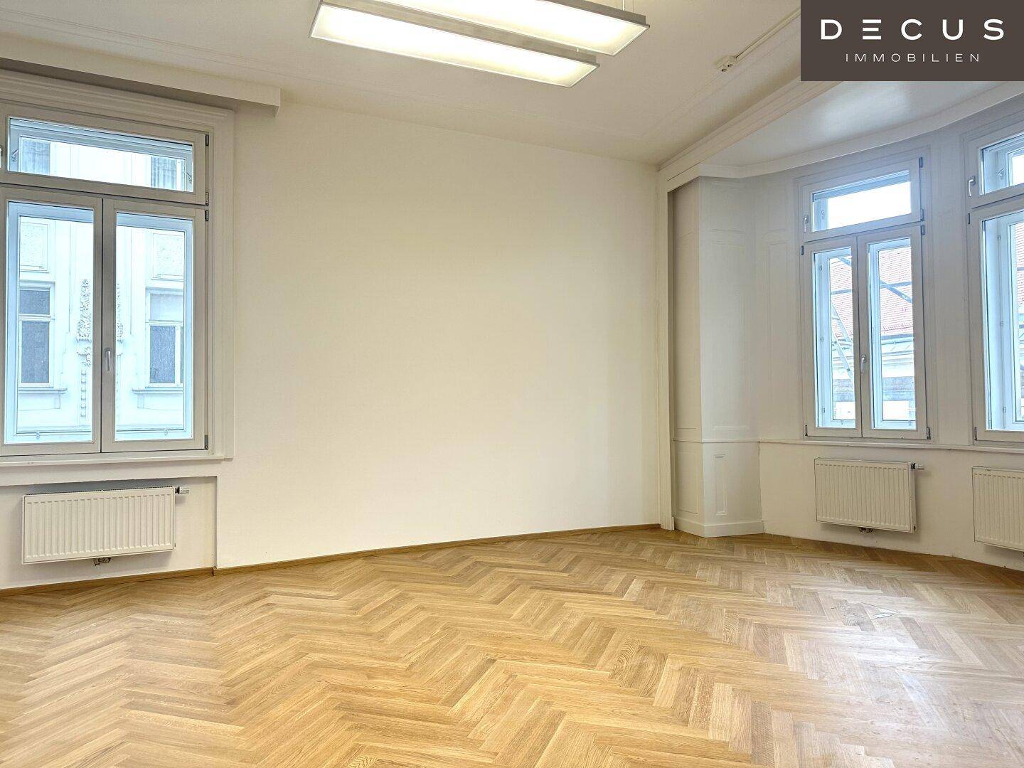 Heller Raum mit Fischgrätparkett, hohen Fenstern und Heizkörpern, bietet eine angenehme Atmosphäre.
