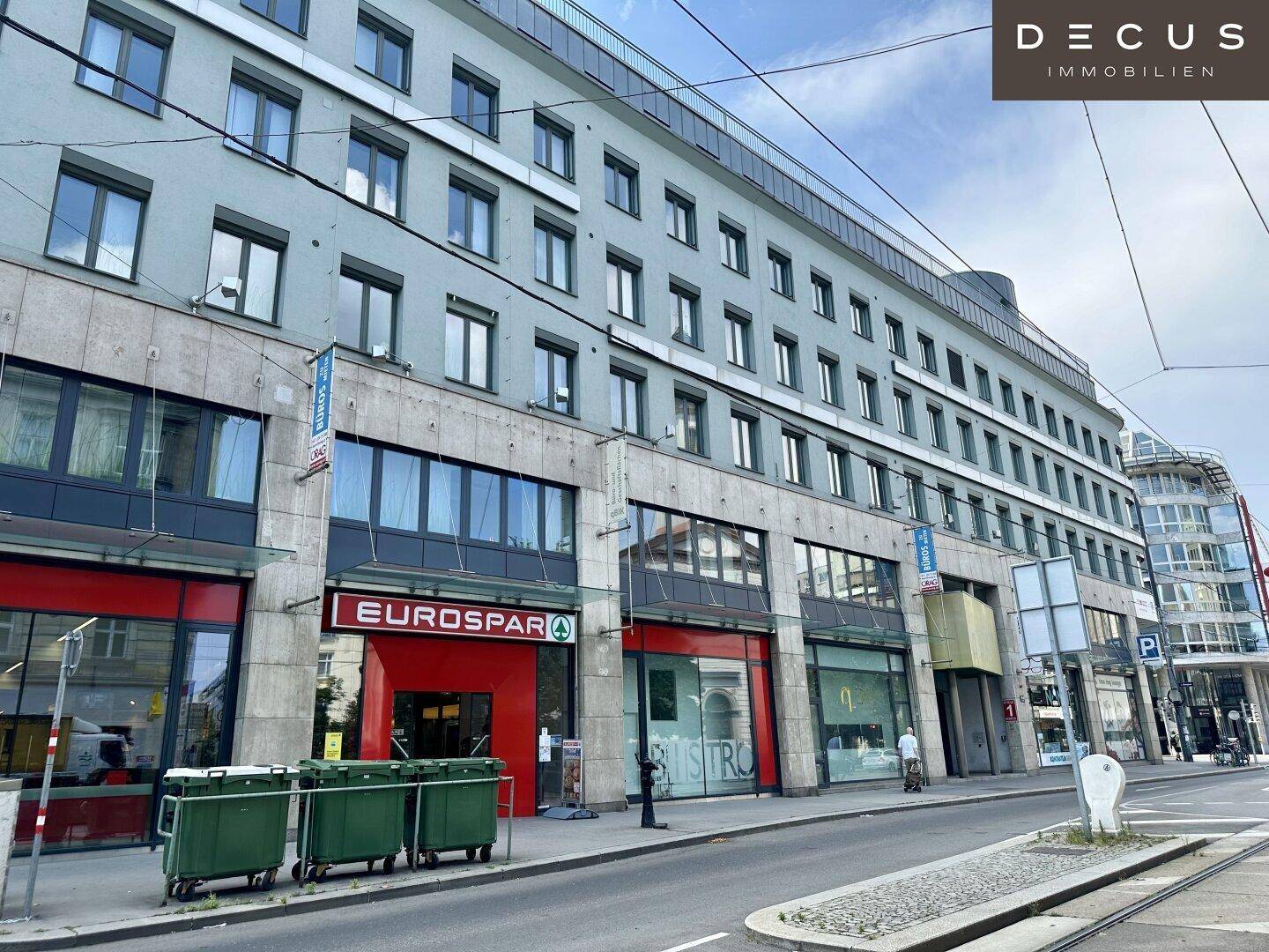 Ansicht der modernen Geschäftsfassade mit verschiedenen Ladenlokalen, darunter ein Supermarkt im Erdgeschoss.