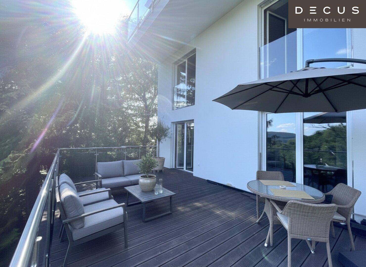 Sonnige Terrasse mit Loungemöbeln und Esstisch, umgeben von grüner Natur.