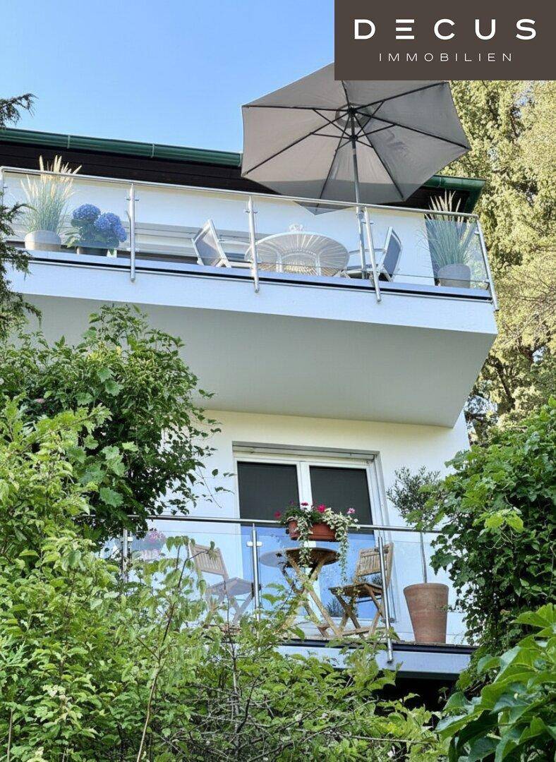 Balkon mit Glasgeländer, Sonnenschirm und einem schönen Blick auf die grüne Umgebung.