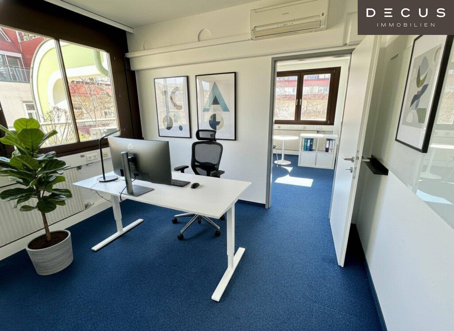 Helles Büro mit Schreibtisch, Bürostuhl und Blick auf die Umgebung durch große Fenster.