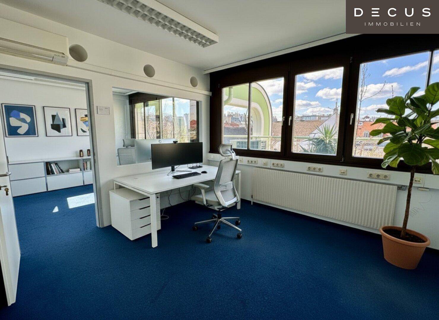 Helles Büro mit blauem Teppichboden, modernem Schreibtisch und Blick auf die Stadt.