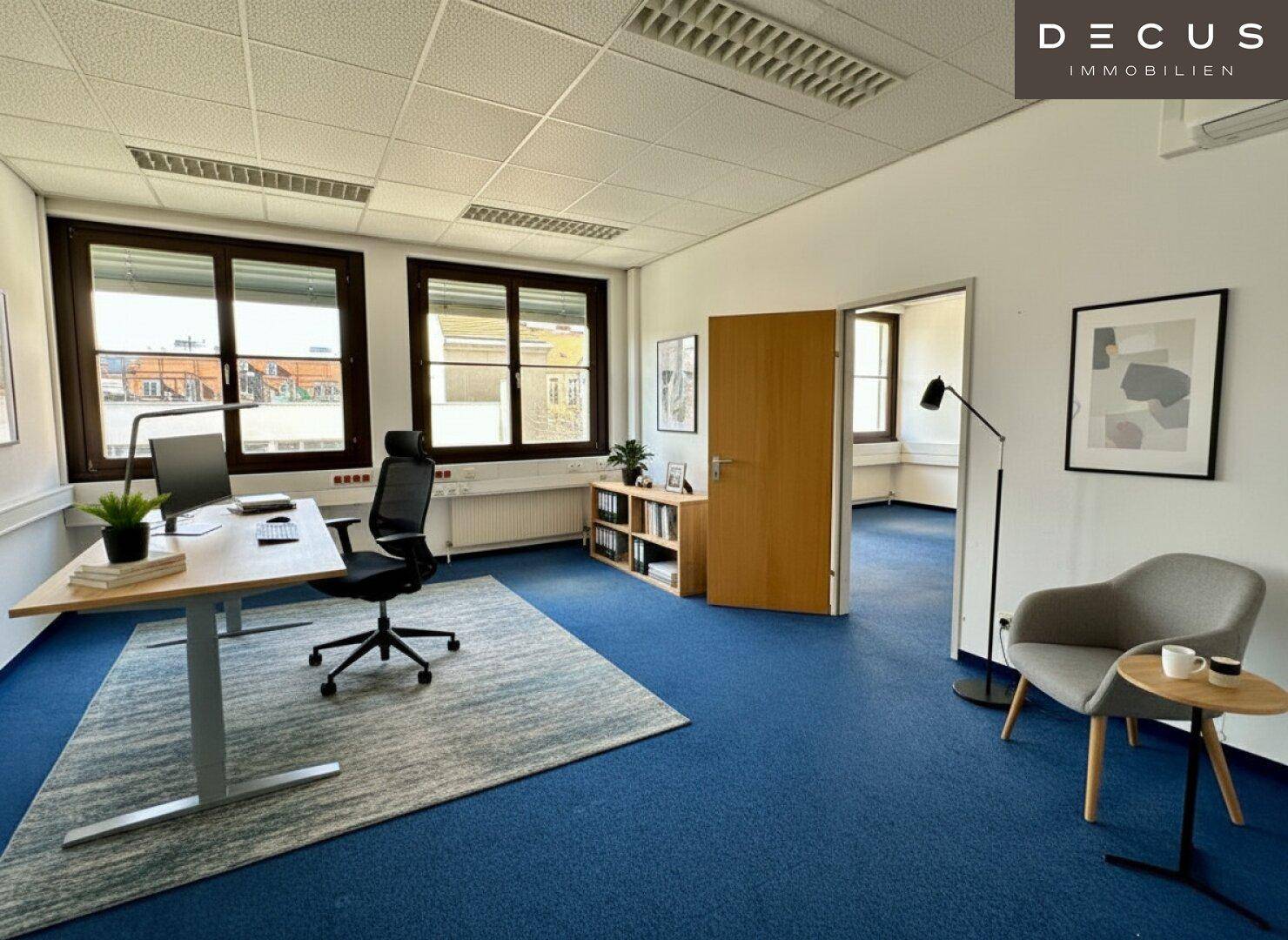 Helles Büro mit blauem Teppichboden, modernem Schreibtisch und bequemen Sitzgelegenheiten.