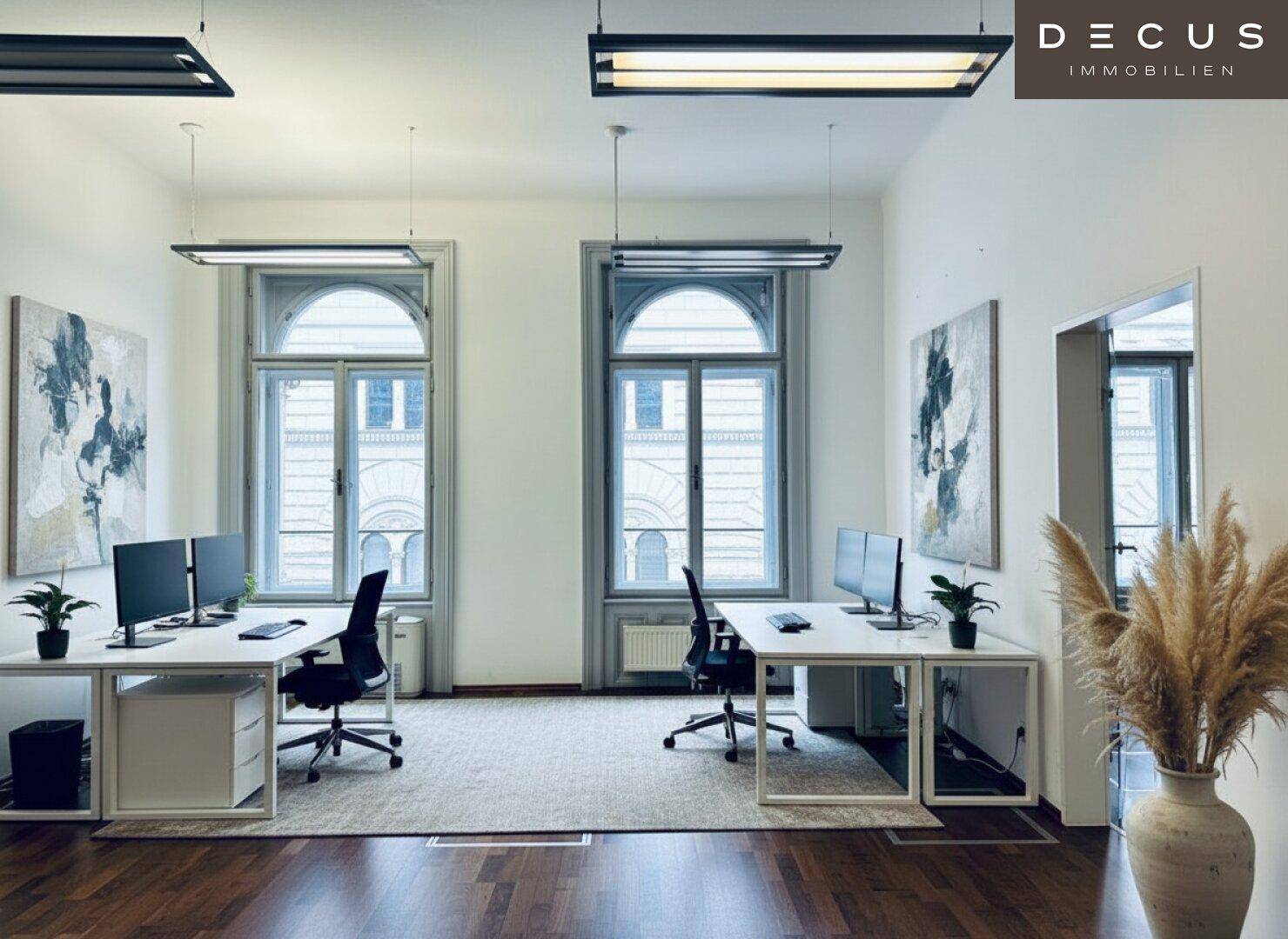 Modern eingerichtetes Büro mit zwei Arbeitsplätzen, Holzboden und großen Fenstern.