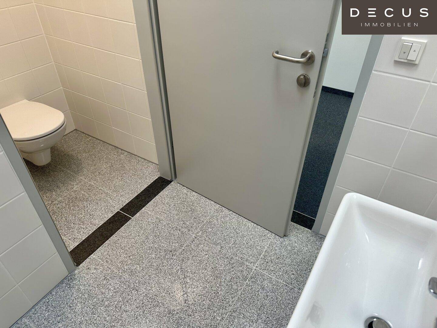 Saubere Toilette mit weißen Fliesen und einem kleinen Waschbecken, funktional und gepflegt.