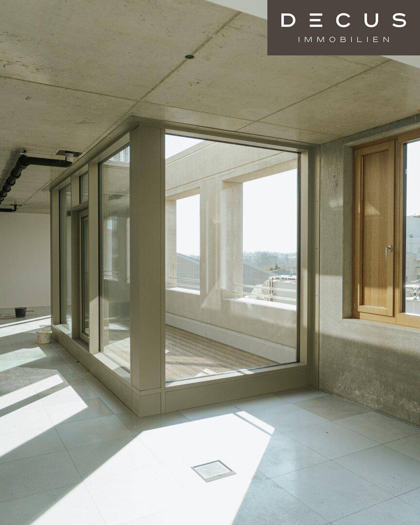 Heller Innenraum im Rohbau mit großen Fenstern und Zugang zu einem Balkon oder einer Loggia.