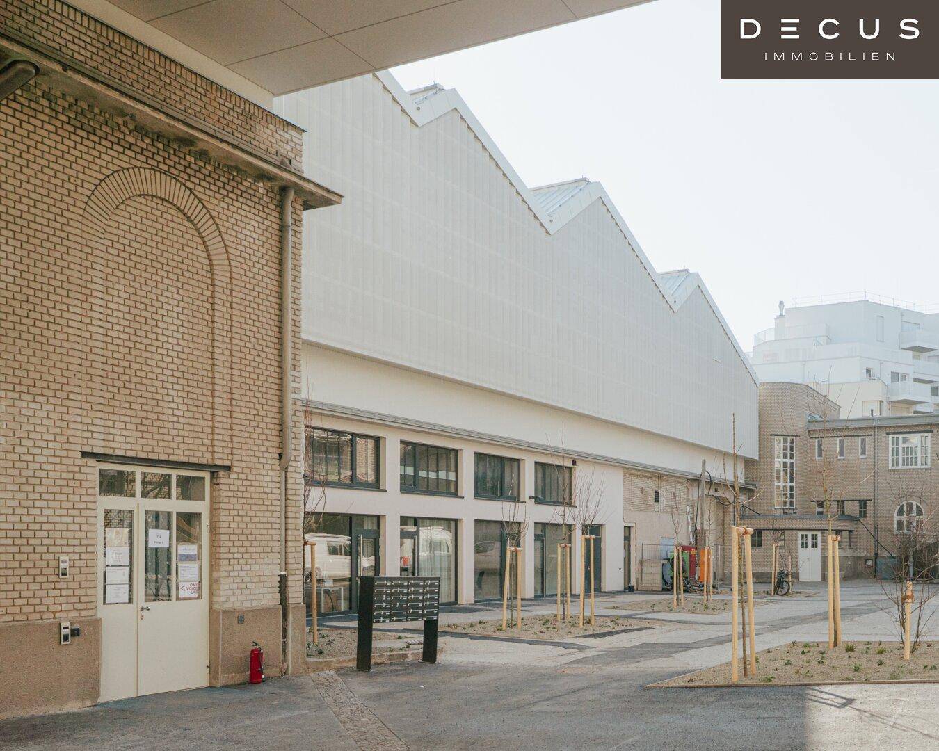Außenansicht eines Gebäudekomplexes mit einem alten Backsteingebäude und einem modernen Neubau mit Sägezahndach.